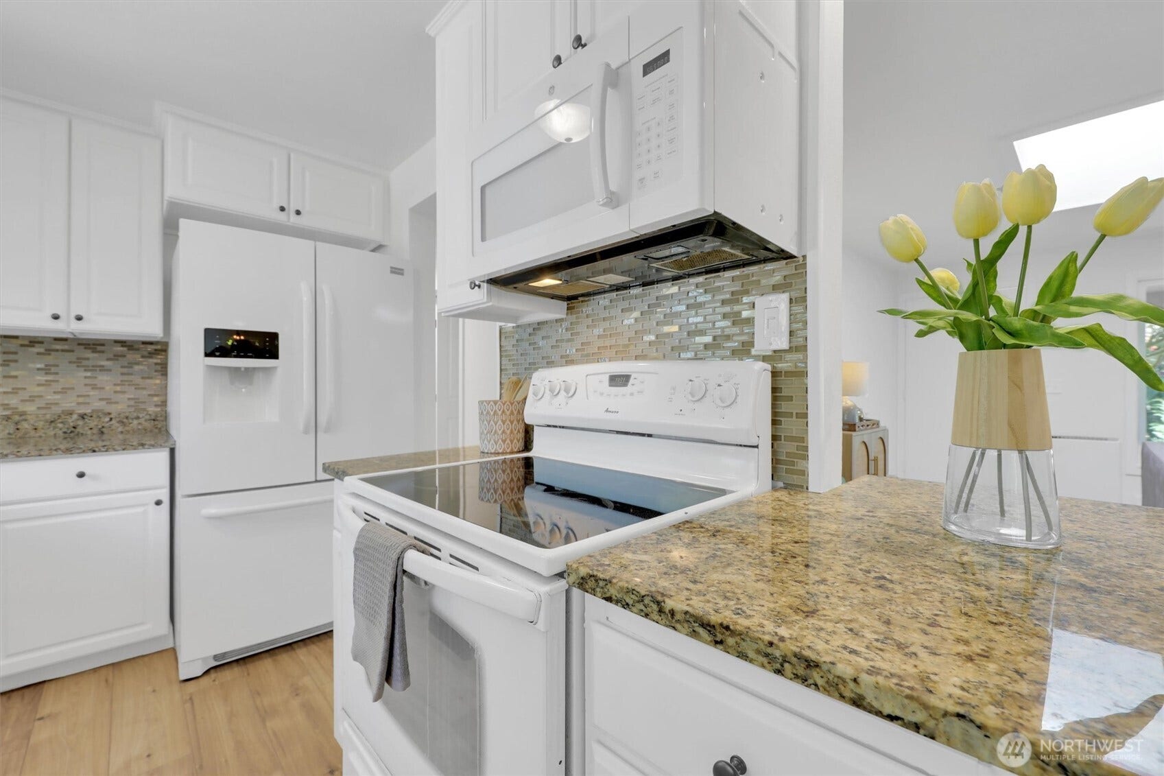 20915 W Richmond Road, Bothell, WA 98021 Kitchen view showcasing granite counter space, white cabinets, modern appliances, mosaic backsplash, and a sunny dining area.