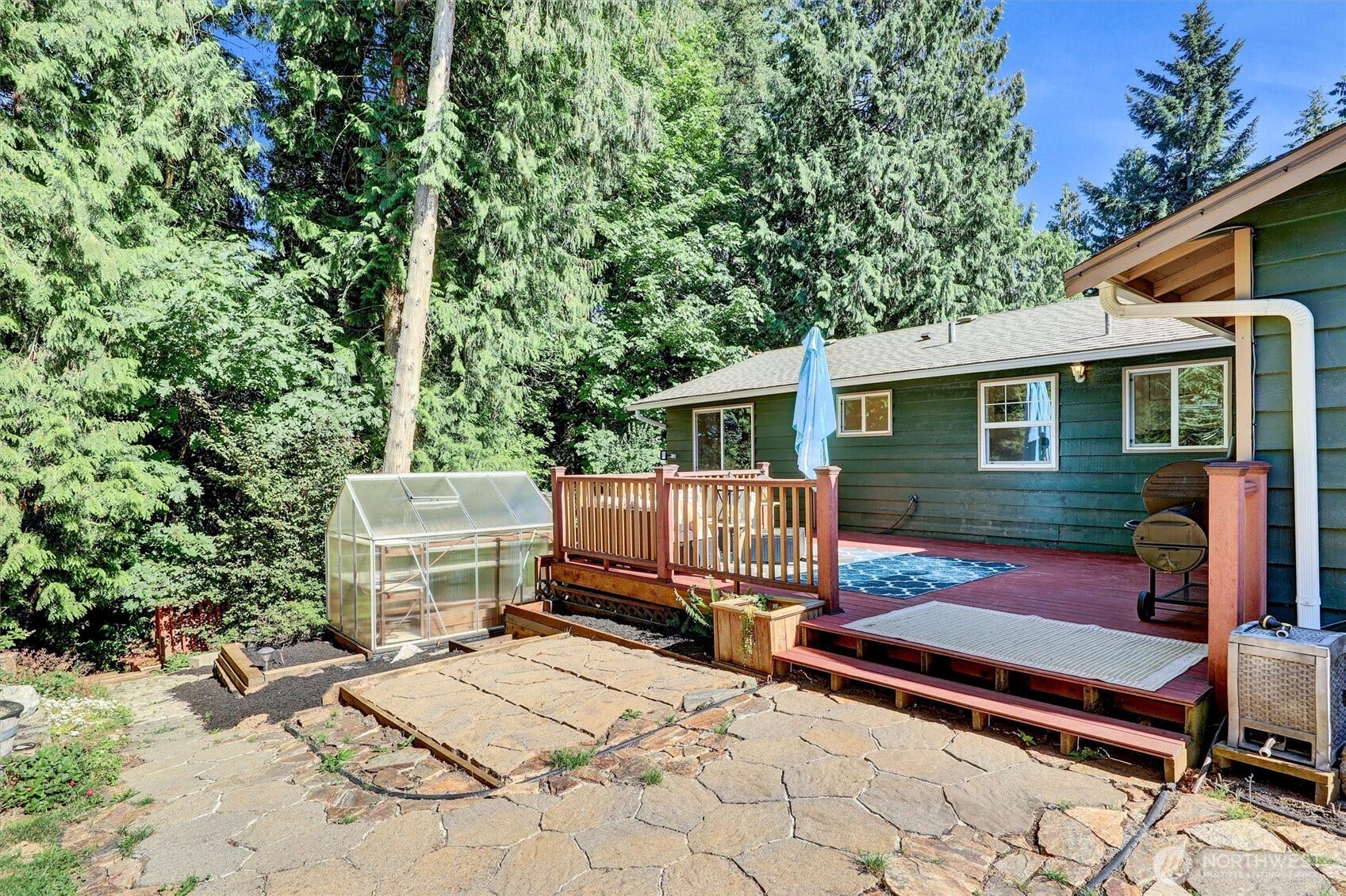 20915 W Richmond Road, Bothell, WA 98021 Rear exterior view showcasing the raised wood deck, greenhouse, outdoor stairs, landscaped yard, and mature evergreen trees.