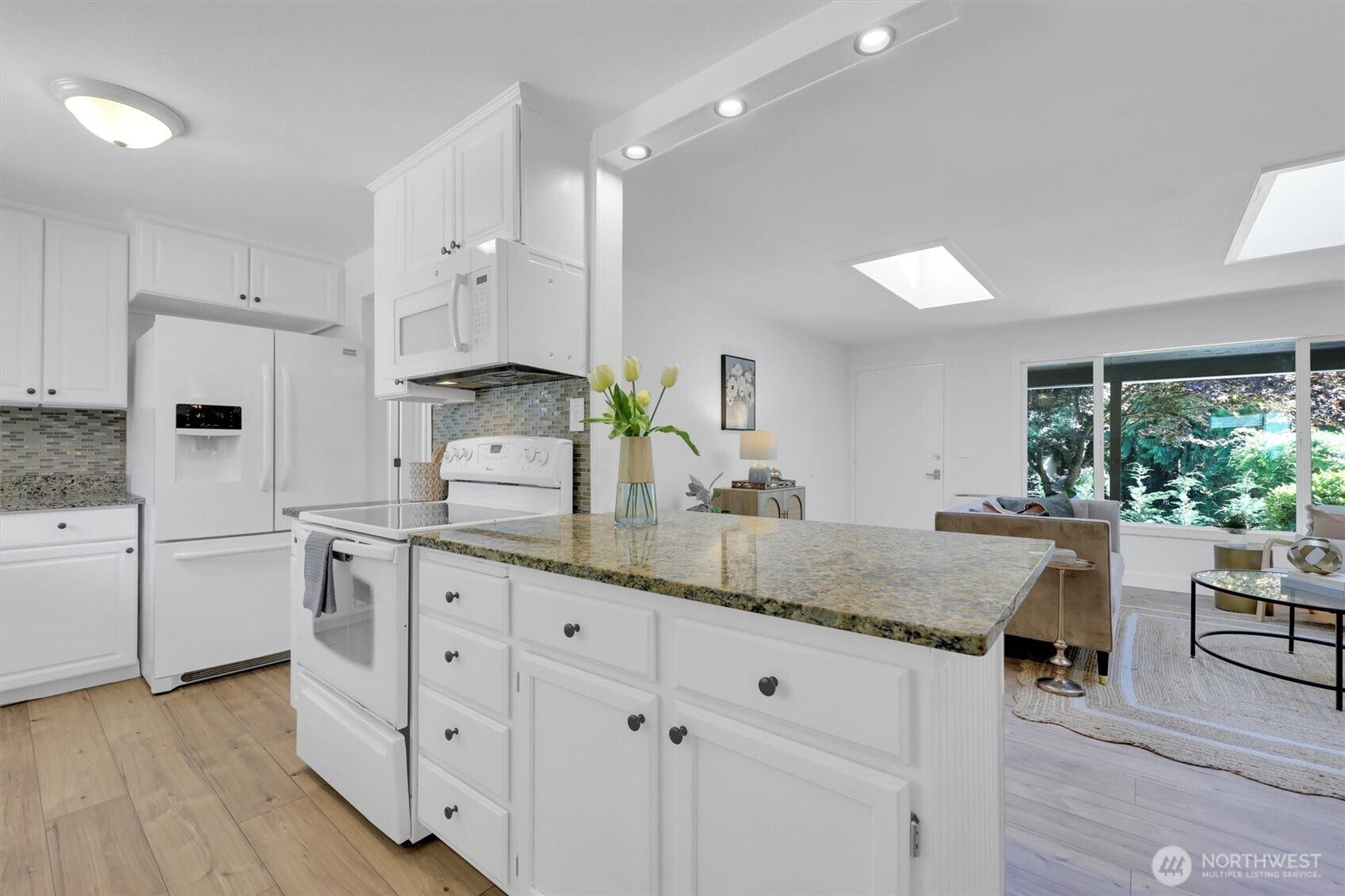 20915 W Richmond Road, Bothell, WA 98021 Spacious kitchen and open-concept living area featuring a large granite island, white cabinetry, hardwood floors, and expansive windows.