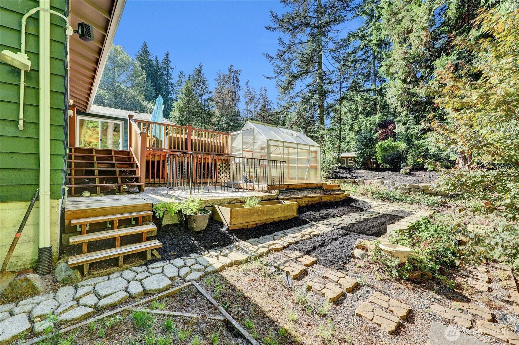 20915 W Richmond Road, Bothell, WA 98021 Backyard view featuring the raised deck, greenhouse, landscaped pathways, mature trees, and private outdoor setting.