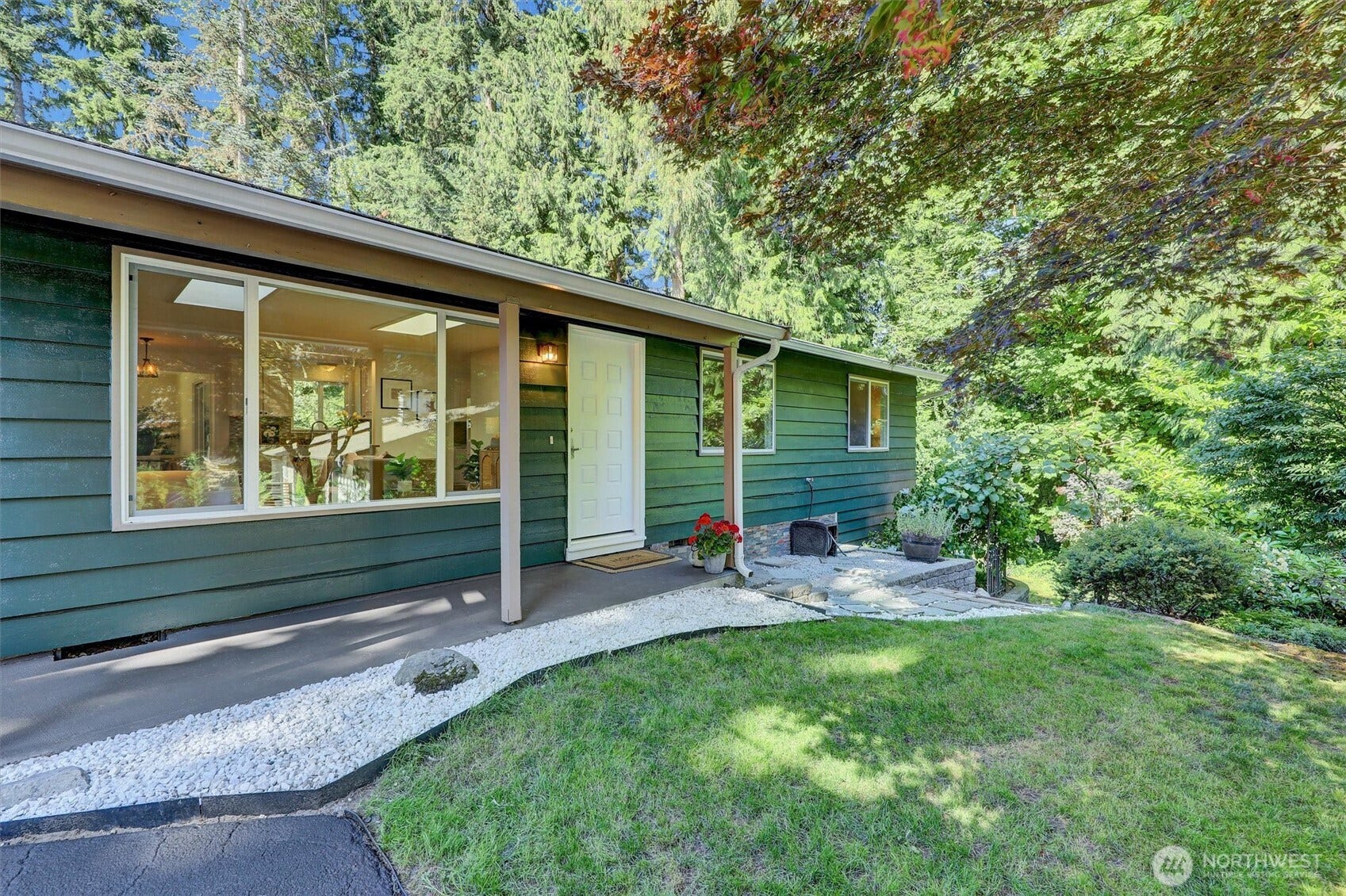 20915 W Richmond Road, Bothell, WA 98021 Side exterior view of the Bothell home showcasing the covered walkway, large windows, landscaped yard, and wooded surroundings.