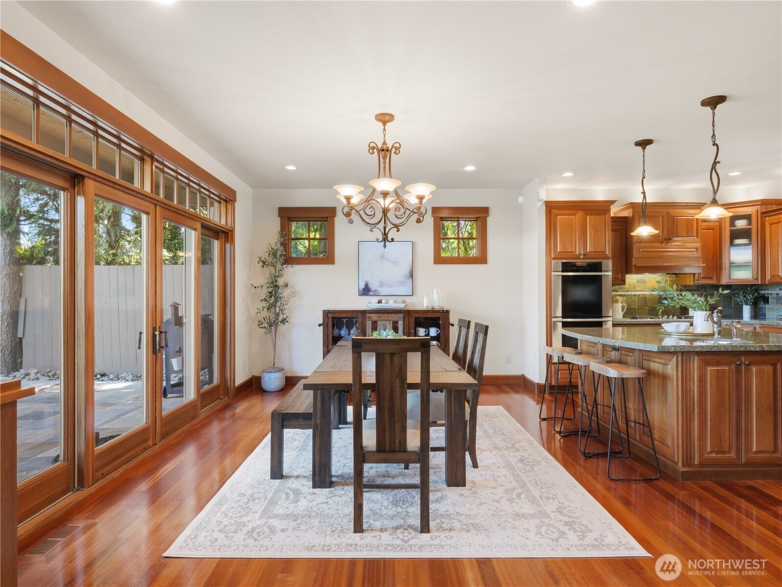 Bright dining space with hardwood floors, elegant lighting, and direct access to outdoor living areas through expansive glass doors.