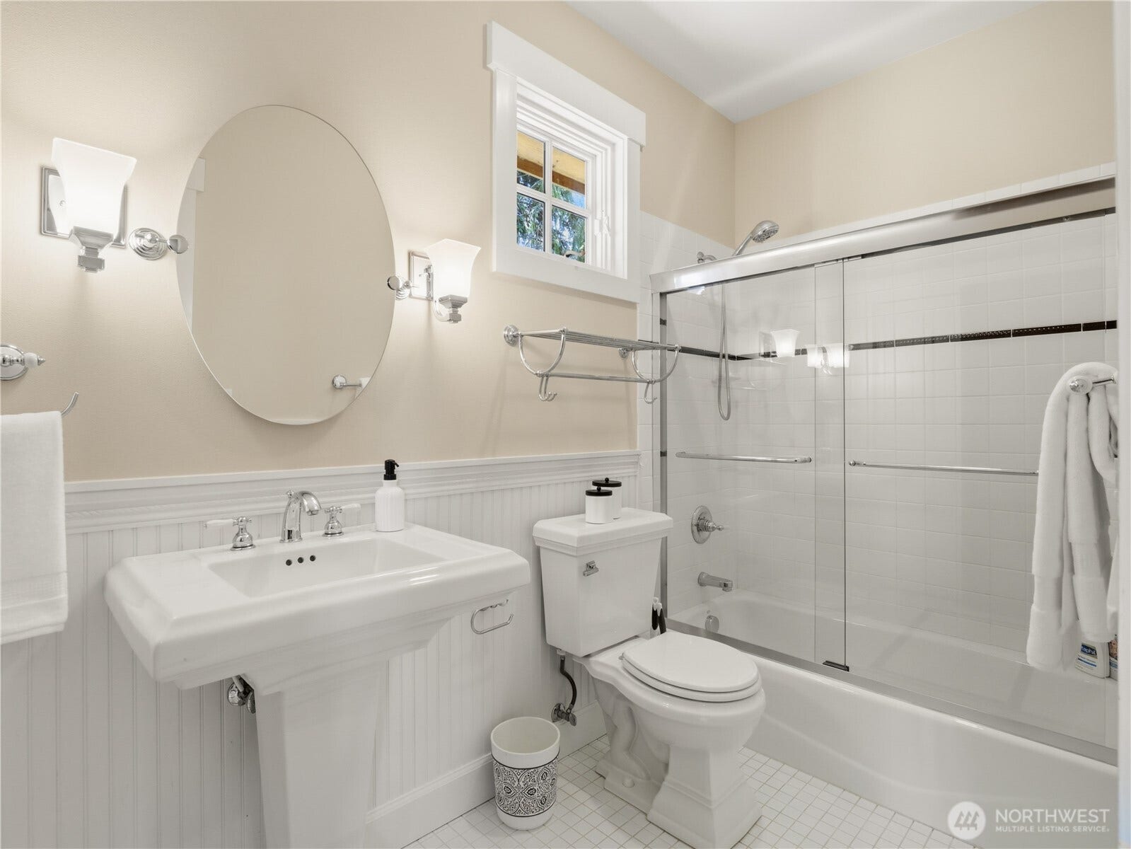 This well-appointed bathroom combines style and functionality with a glass-enclosed tub/shower, crisp tile finishes, and charming architectural details.