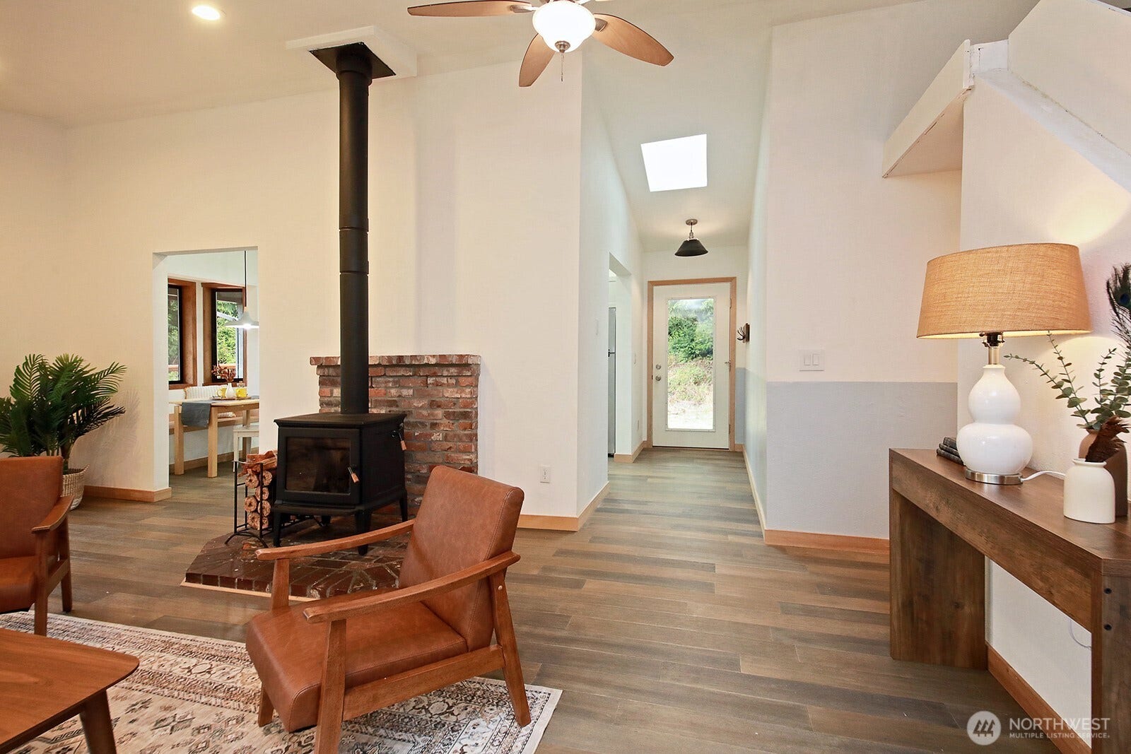 Looking back at the main entrance. The kitchen is through the opening to the left of the entrance or left of the newer wood stove. Hallway to the 2 main level bedrooms and remodeled full bath is along the right edge of the photo (beyond the white lamp).