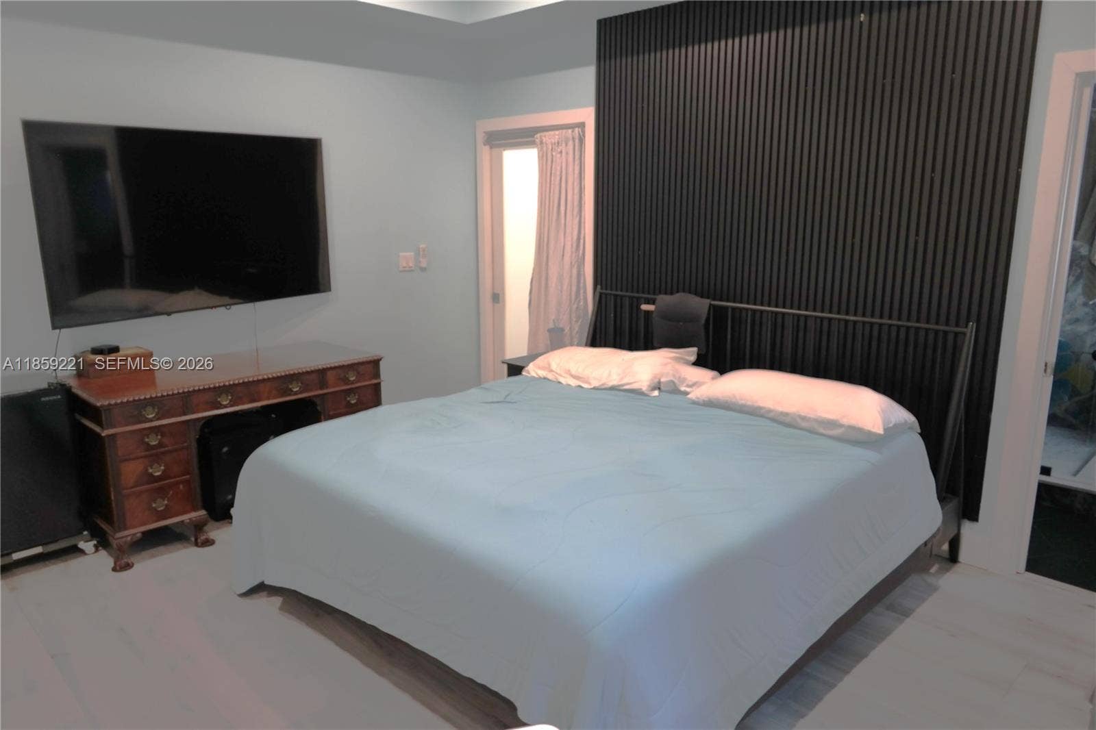 524 NE 27th Drive, Wilton Manors, FL 33334 Spacious master bedroom featuring a ceiling fan, wood-paneled accent wall, private bath, and direct access to the backyard corridor