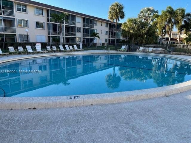 Large heated oval-shaped pool with lounge chairs in a gated area.