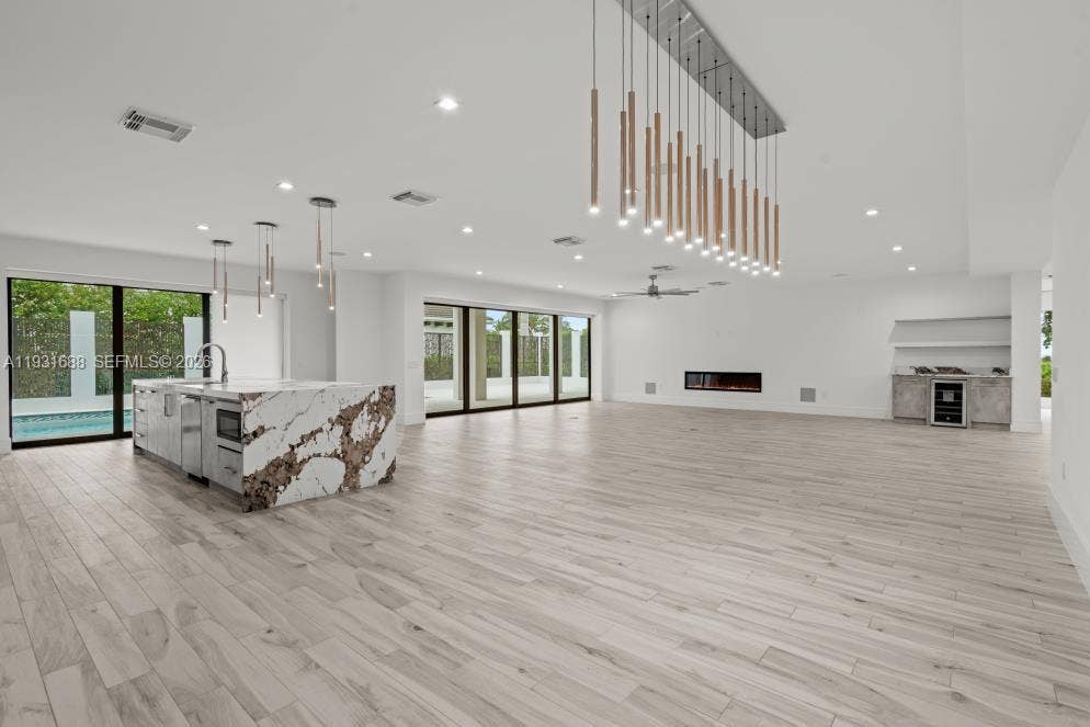 Open-concept space featuring wood-finish flooring, a kitchen island with stone waterfall edges, a linear fireplace, custom pendant lighting, and floor-to-ceiling glass sliding doors