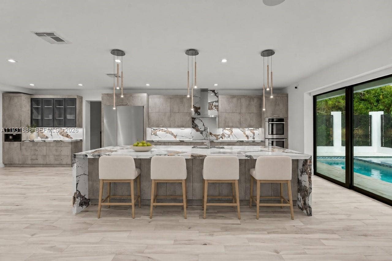 Chef's kitchen featuring flat-panel cabinetry, a waterfall island with stone countertop, built-in stainless steel appliances, and multi-light pendant fixtures