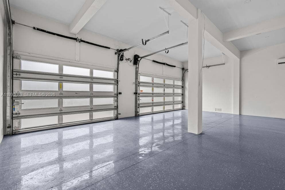 Multi-car garage featuring epoxy-coated flooring, white-finished walls, exposed structural beams, and two overhead metal doors with frosted glass inserts