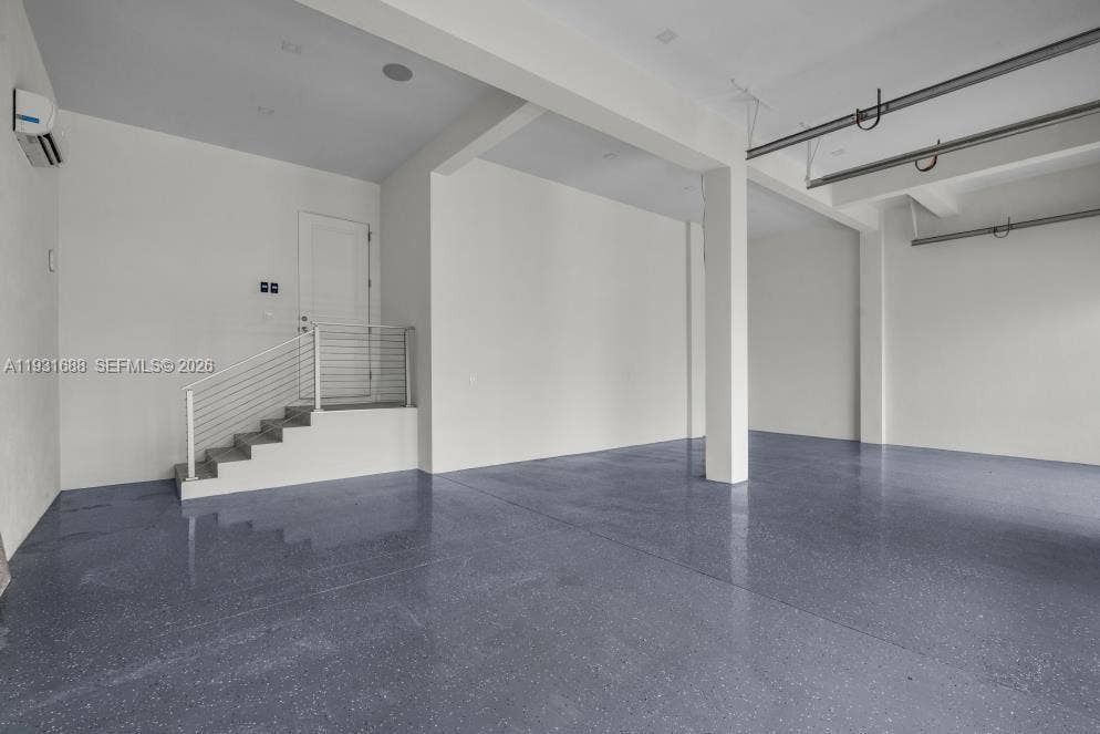 Open-concept interior featuring high ceilings, epoxy-finished flooring, structural support columns, and an elevated staircase with horizontal cable railing
