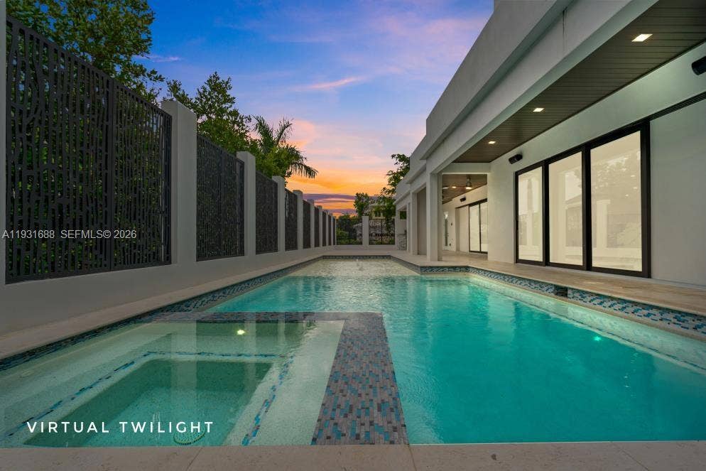 In-ground swimming pool with integrated spa, mosaic tile detailing, expansive patio, and decorative metal perimeter screening
