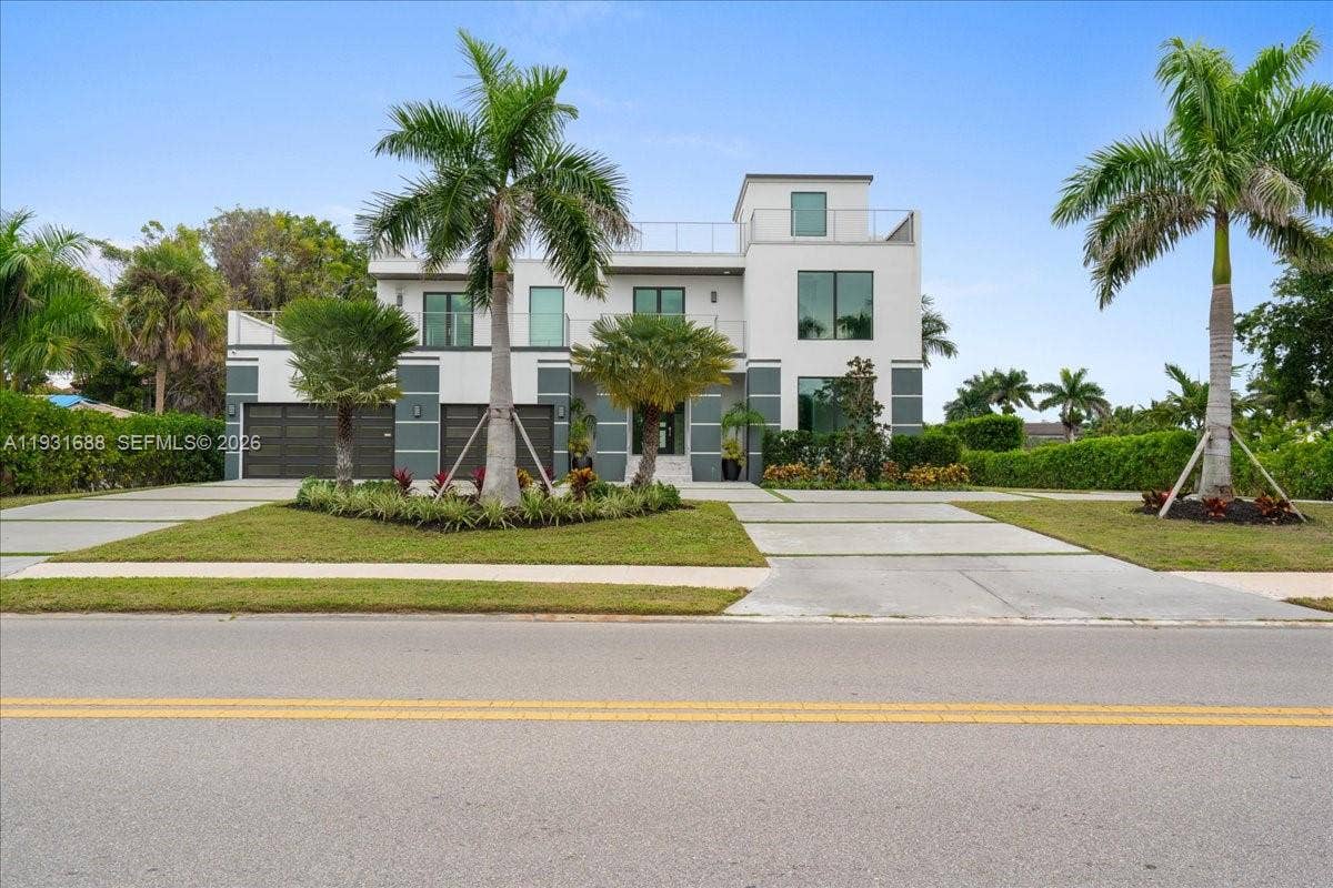 Modern two-story exterior featuring multi-level balconies, expansive multi-pane windows, a split three-car garage, and a concrete paver driveway
