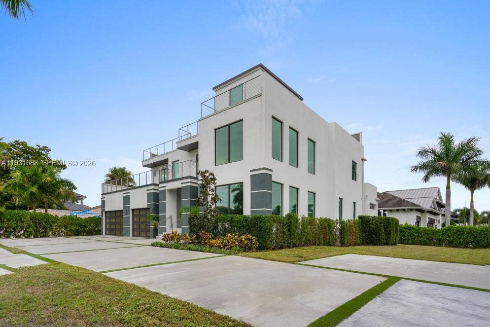 Modern multi-level exterior featuring white stucco facade, full-height windows, tiered balconies with glass railings, and a concrete driveway