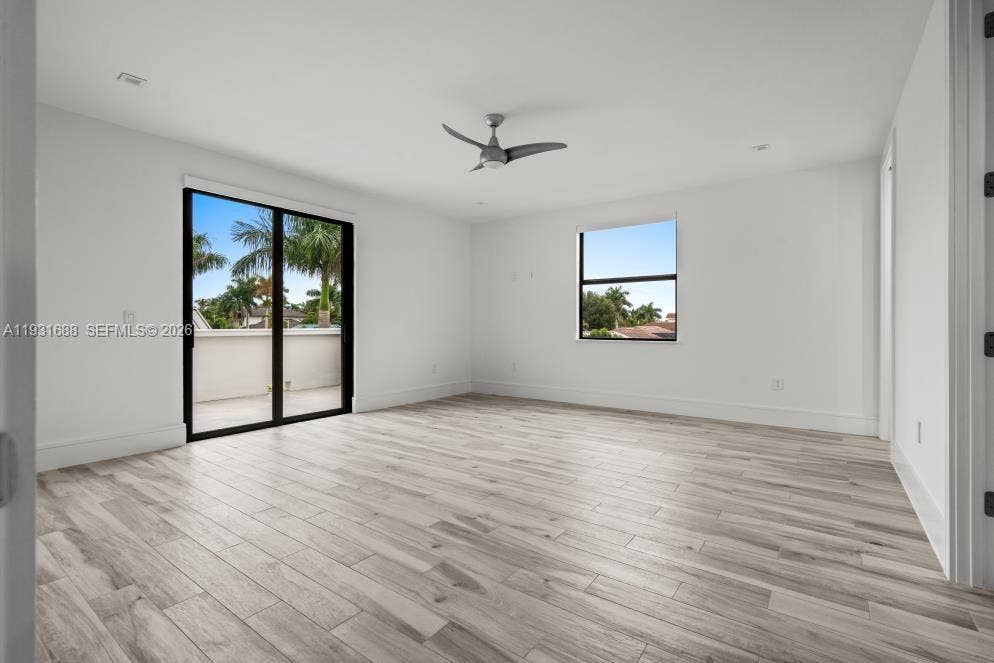 Neutral-toned wood-finish flooring, recessed lighting, multi-blade ceiling fan, sliding glass doors, and window with exterior palm tree scenery