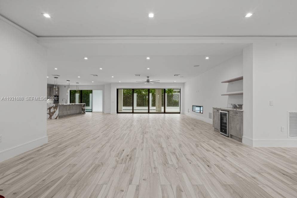 Open-concept interior featuring wood-finish flooring, recessed lighting, multi-panel sliding glass doors, a built-in beverage center, and a horizontal wall-integrated fireplace
