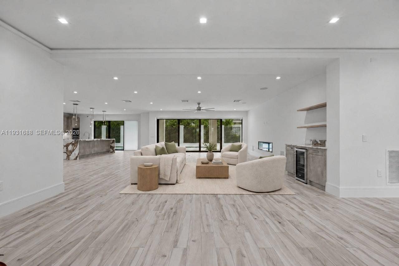 Open-concept interior featuring wood-finish flooring, recessed lighting, multi-panel sliding glass doors, a linear fireplace, and a built-in wet bar with a beverage refrigerator