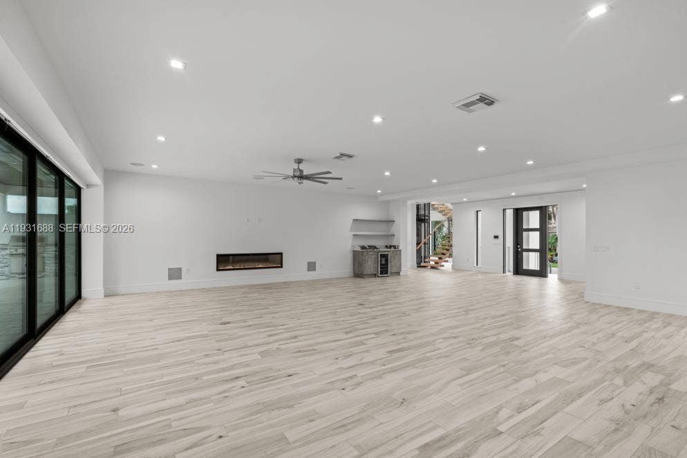 Open-concept interior featuring wood-finish flooring, recessed lighting, a linear fireplace, custom built-in cabinetry with a stone countertop, and multi-panel glass sliding doors