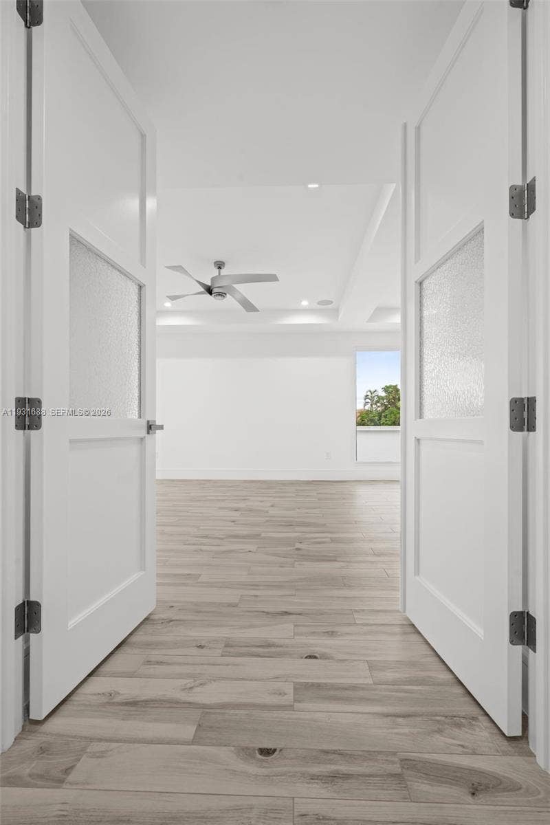 Double doors with frosted glass inserts featuring wood-finish flooring, a tray ceiling, and a ceiling fan