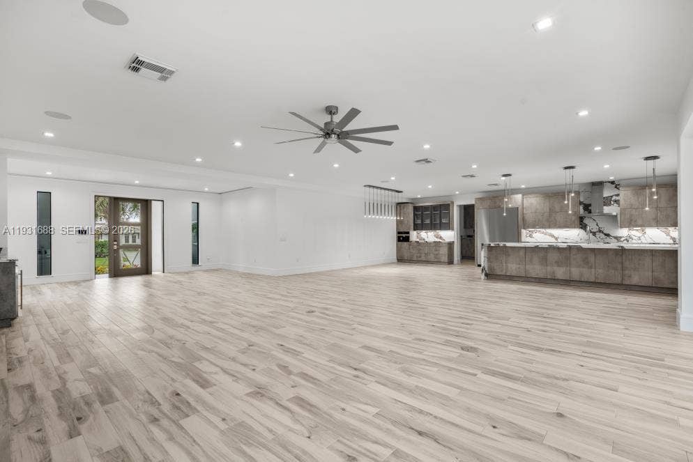 Open-concept interior featuring light wood-finish flooring, recessed lighting, a modern ceiling fan, and a kitchen equipped with stone-patterned backsplashes and integrated cabinetry