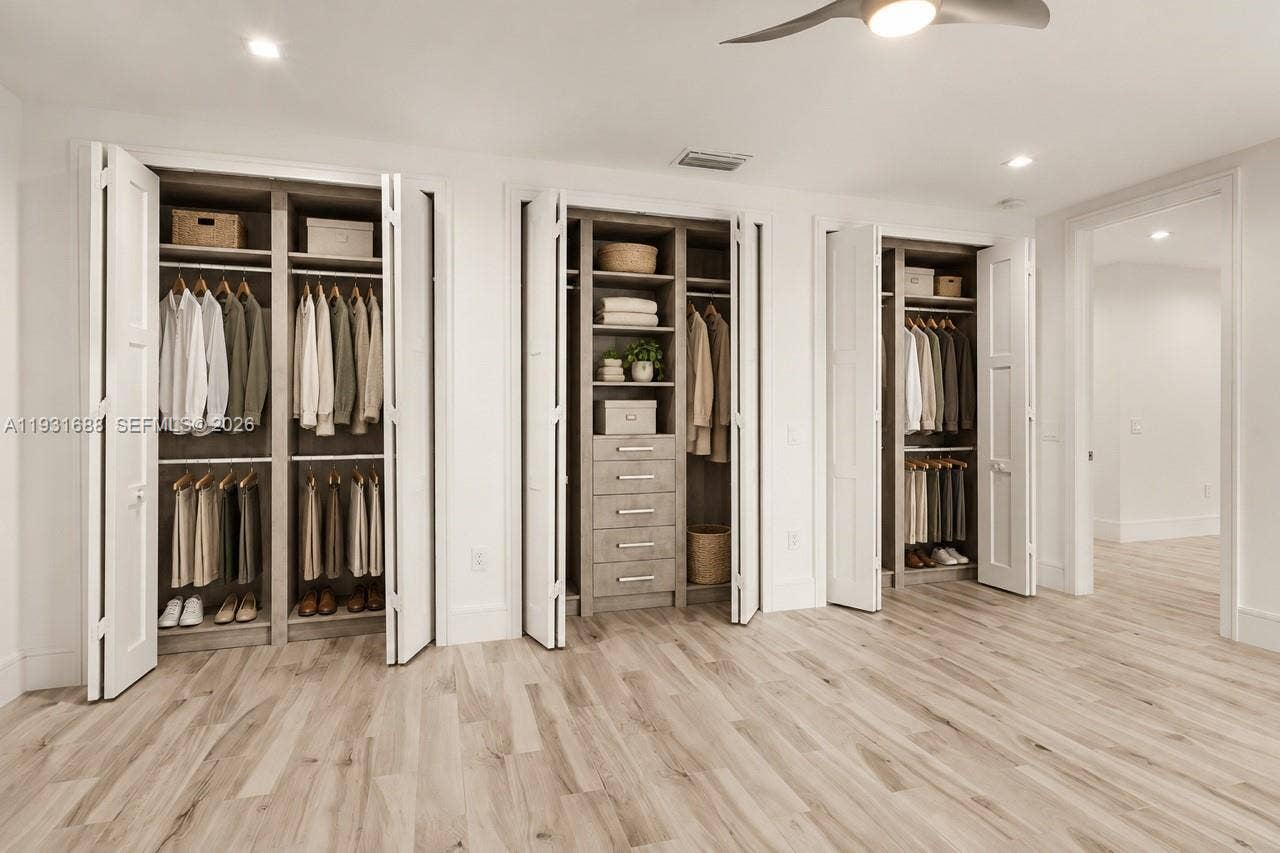 Custom built-in closet system featuring multi-tiered hanging rods, open shelving, integrated drawers with horizontal pulls, and bifold doors set against wood-finish flooring