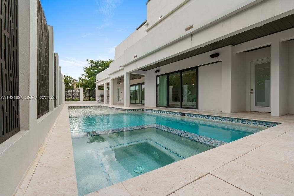 In-ground swimming pool with an integrated spa, stone-tile decking, covered patio area, and architectural privacy screens