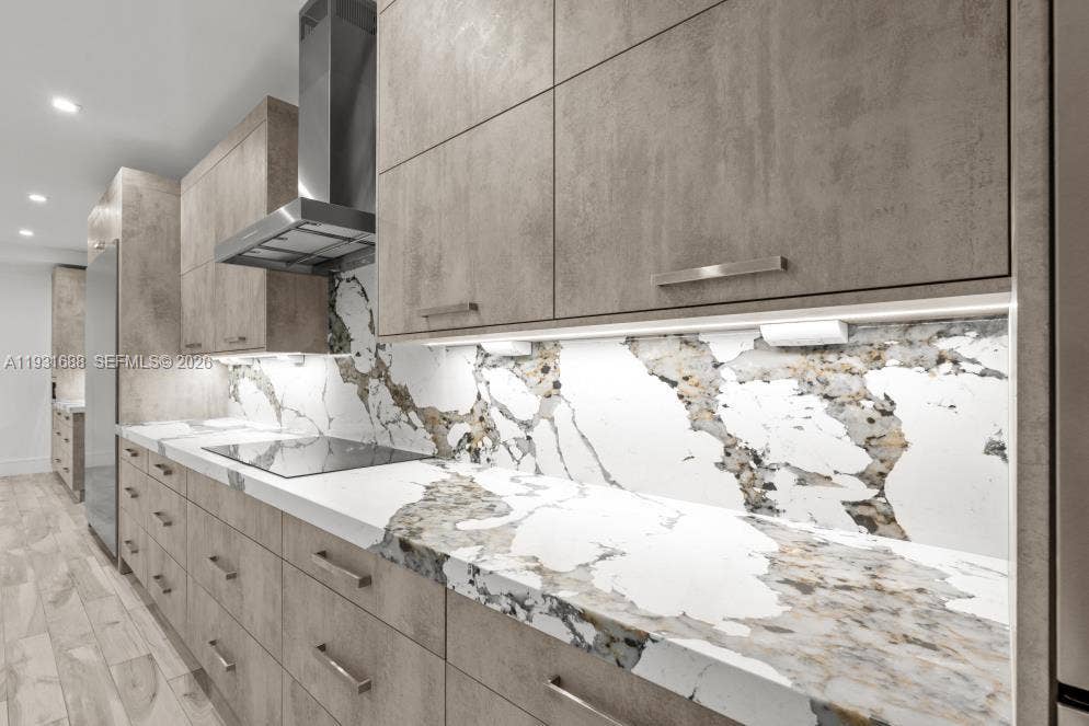Modern kitchen featuring matte-finish cabinetry, patterned stone-surface countertops with a matching full-height backsplash, stainless steel range hood, and integrated under-cabinet lighting
