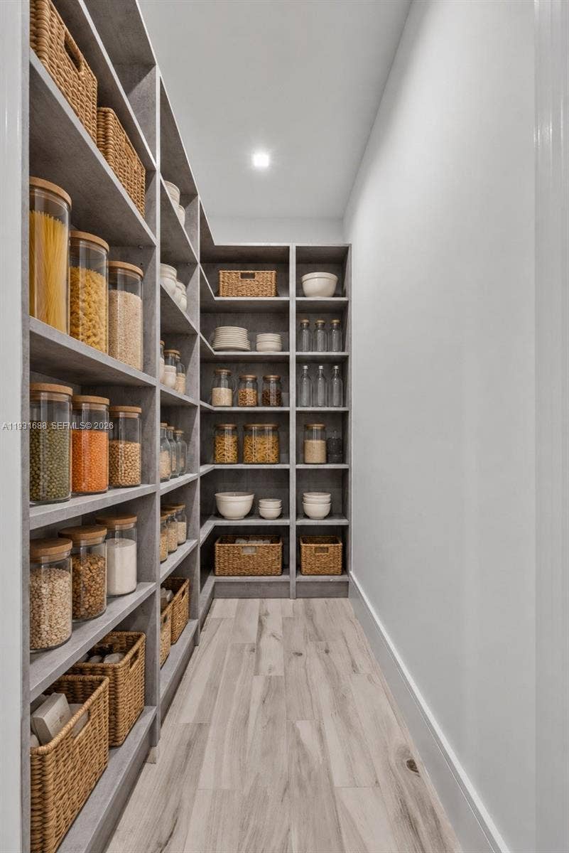Walk-in pantry featuring floor-to-ceiling built-in shelving, gray cabinetry, and wood-finish flooring