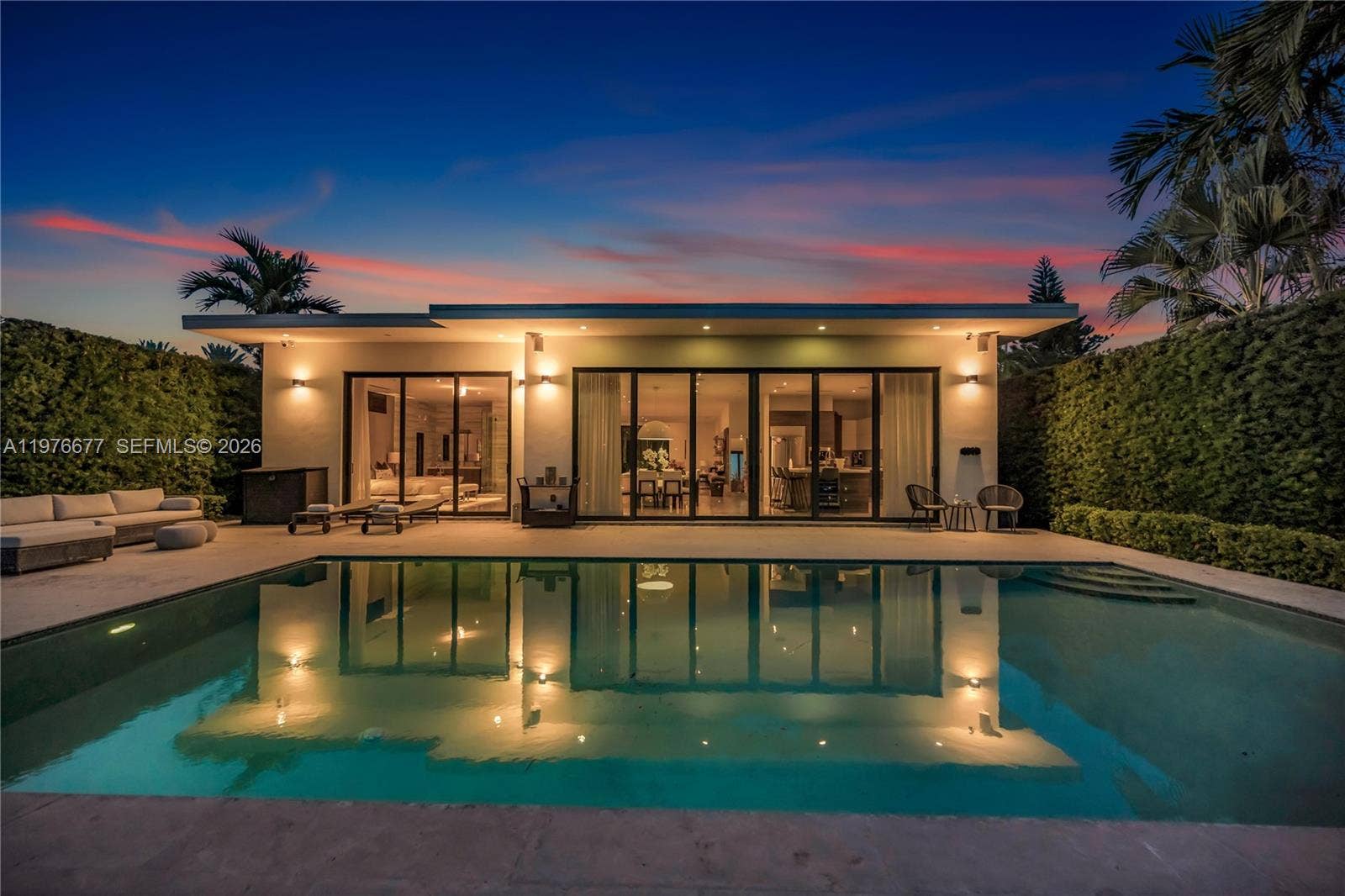 Modern residence featuring a swimming pool, expansive stone patio, flat roofline, and multi-panel glass sliding doors