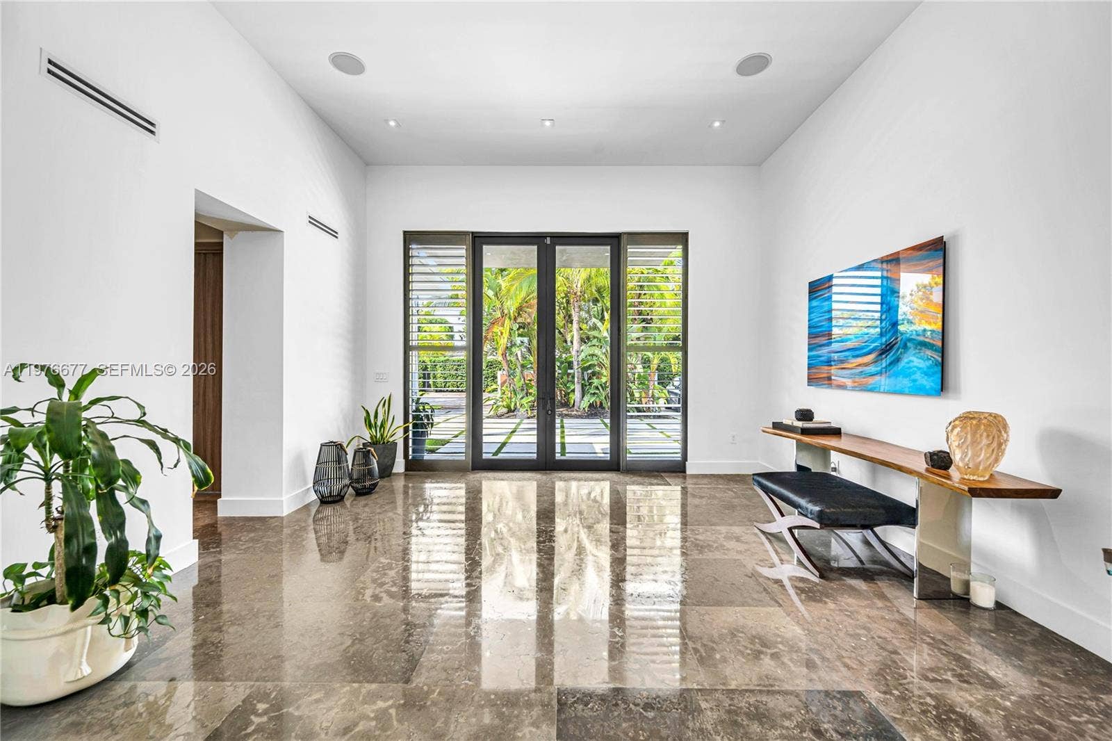 Grand entryway featuring high ceilings, polished stone flooring, recessed lighting, and expansive glass-paned double doors with integrated shutters