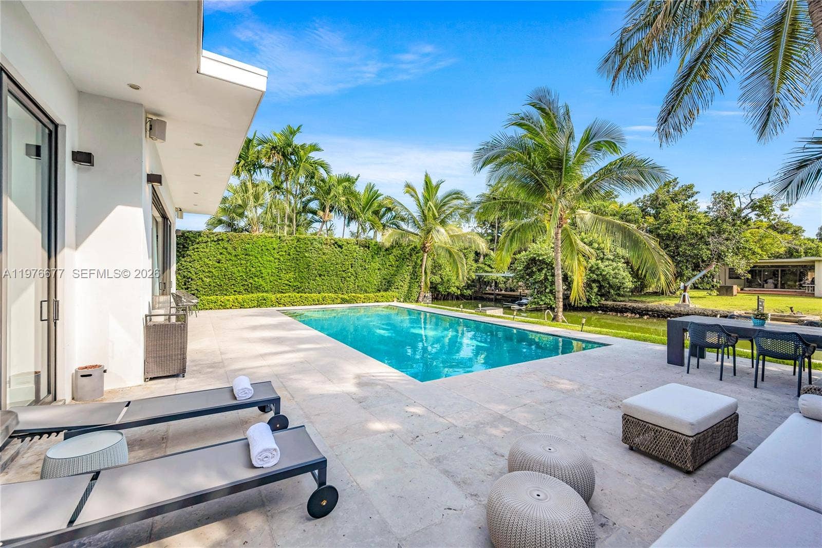 Outdoor terrace featuring stone pavers, a rectangular swimming pool, and manicured perimeter hedging