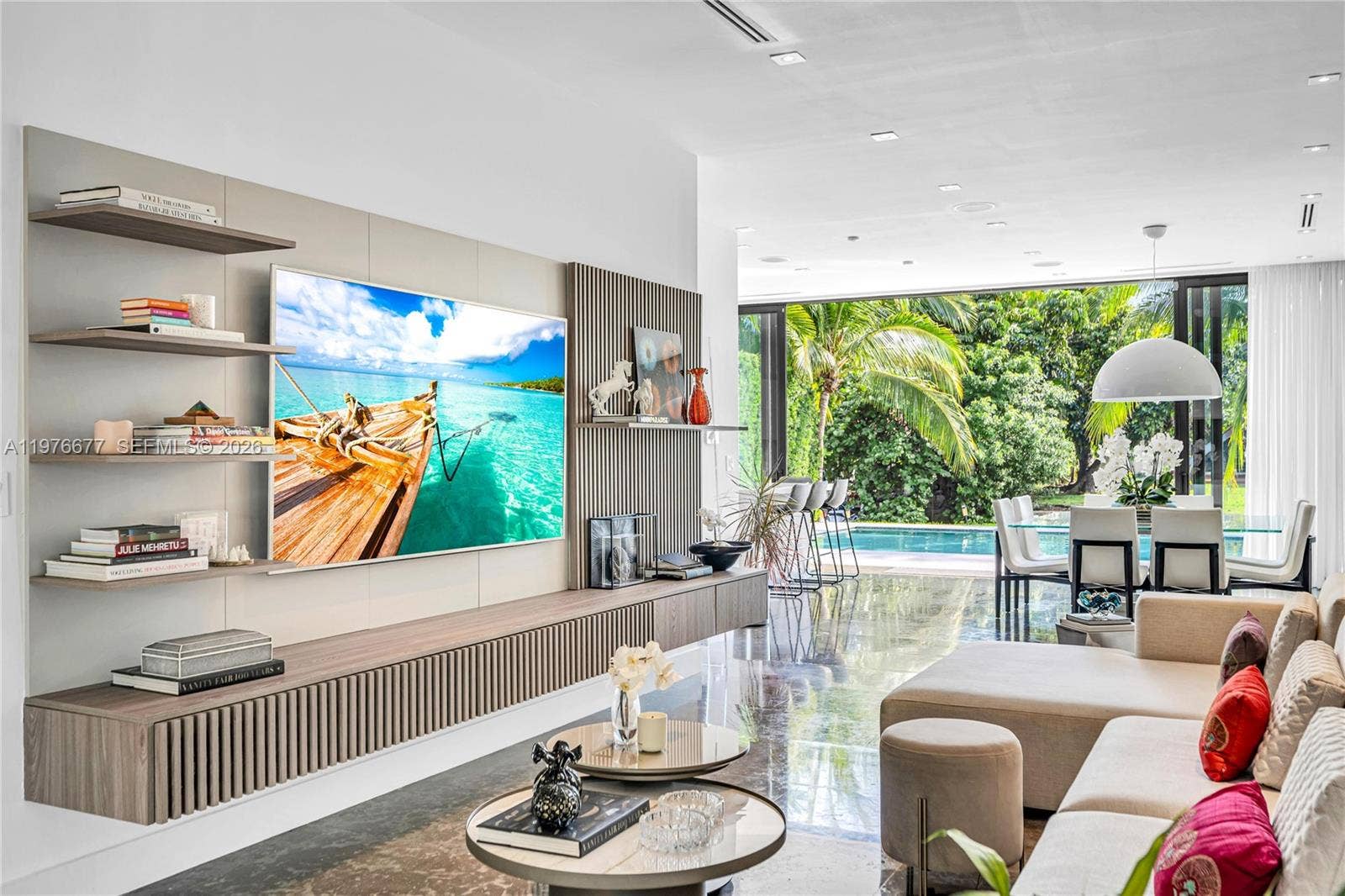 Custom wall-mounted media console with fluted wood-finish cabinetry, integrated open shelving, recessed ceiling lighting, polished stone flooring, and expansive multi-panel glass doors