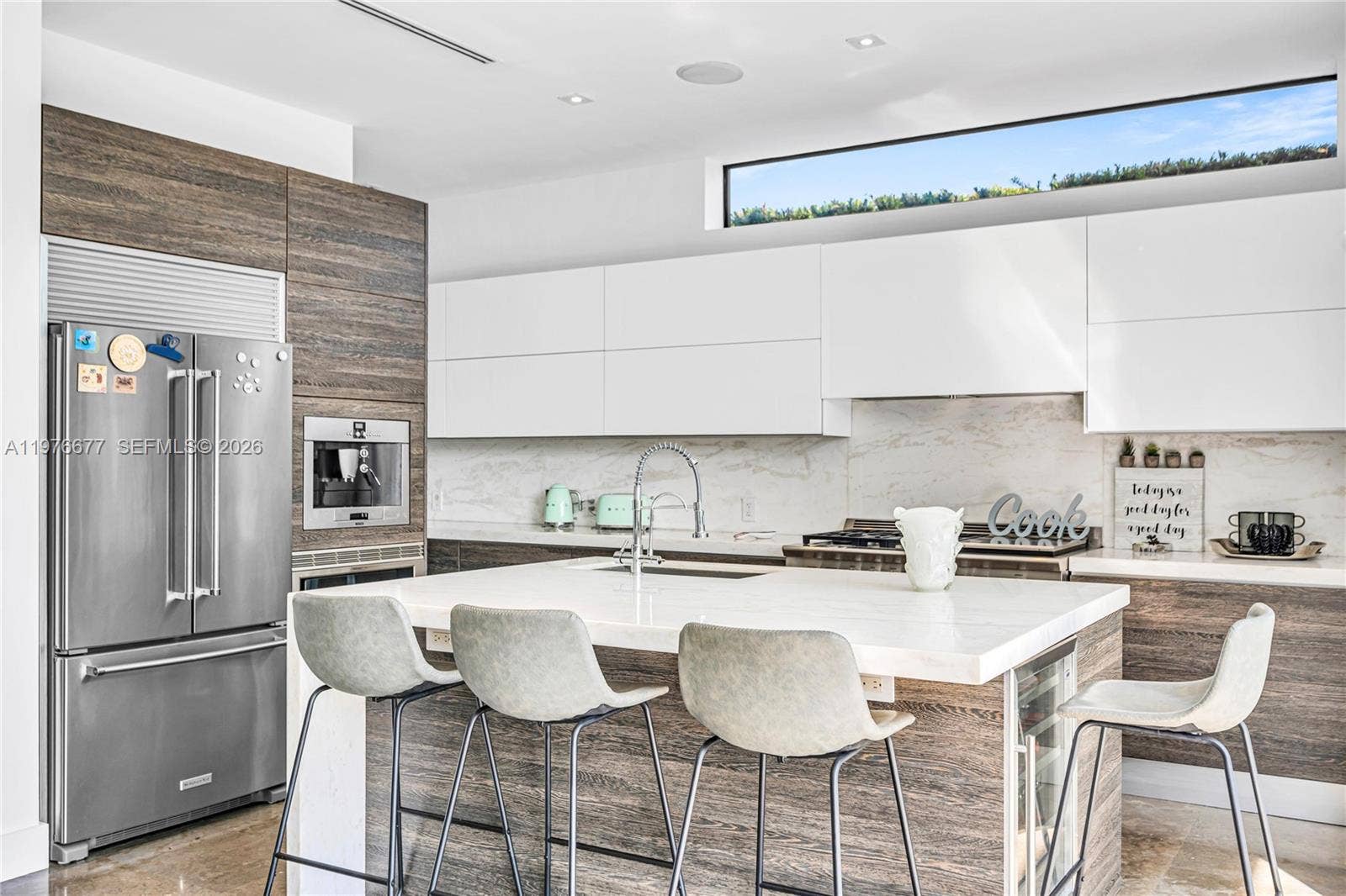 Kitchen featuring flat-panel white cabinetry, wood-finish lower cabinetry, stone-finish countertops, an island with integrated appliances, and a clerestory window