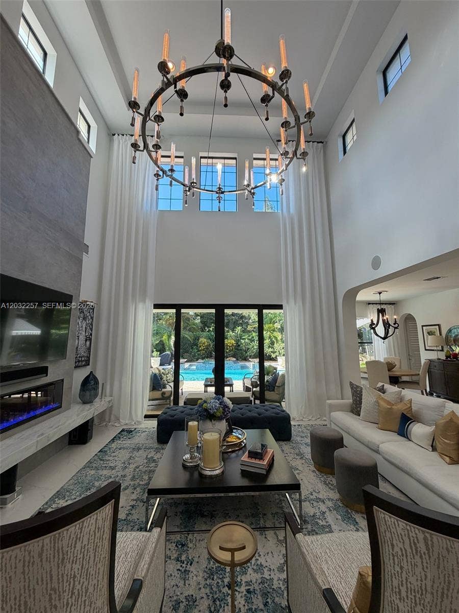 GREAT ROOM HAS FLOOR TO CEILING CUSTOM MADE WINDOW TREATMENTS AND A BEAUTIFUL TILED WALL WITH A FLOATING MARBLE MANTEL SHOWCASING AN ELECTRIC FIREPLACE. VIEWS OF THE RESORT STYLE POOL/SPA AREA.