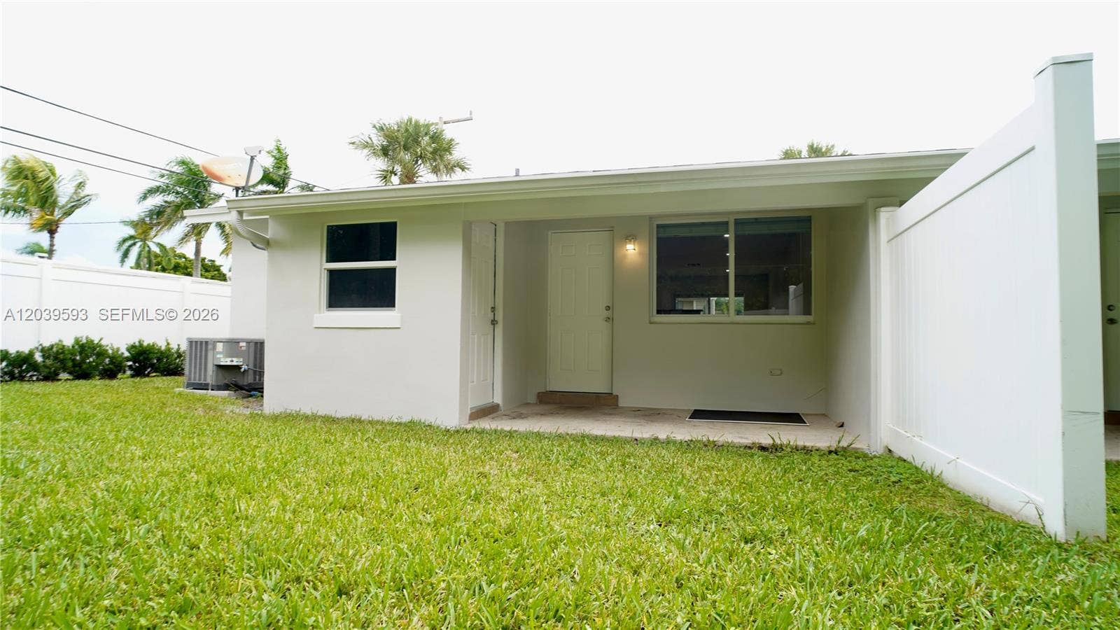 Exterior view featuring a stucco finish, covered porch, white vinyl privacy fencing, and a manicured lawn