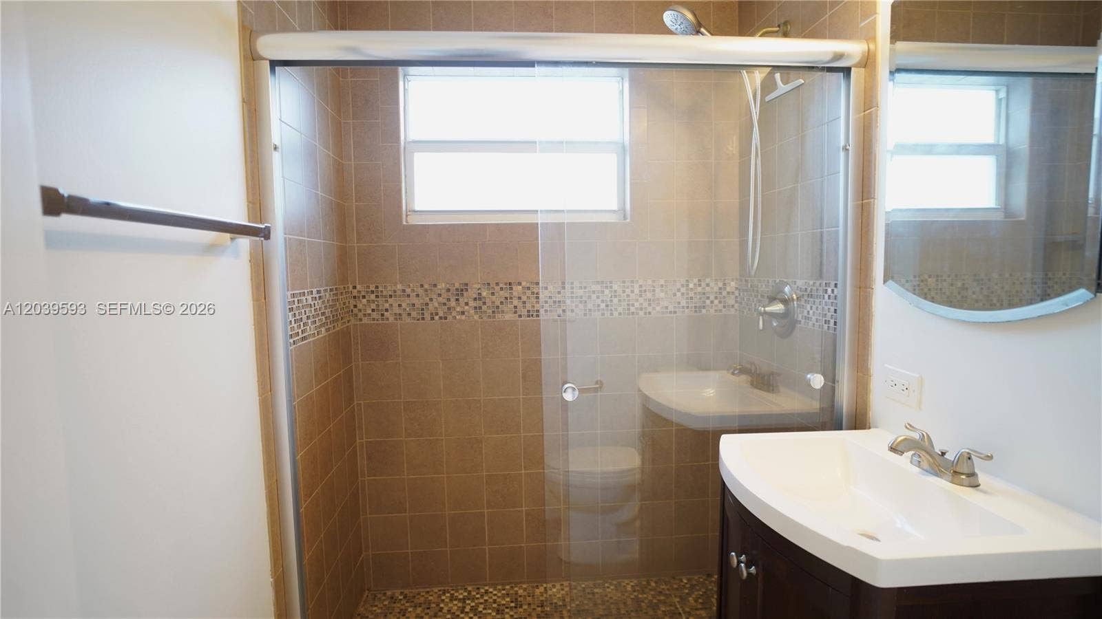 Bathroom featuring a walk-in shower with sliding glass doors, mosaic tile accents, a wall-mounted faucet, a vanity with a white basin, and a framed mirror