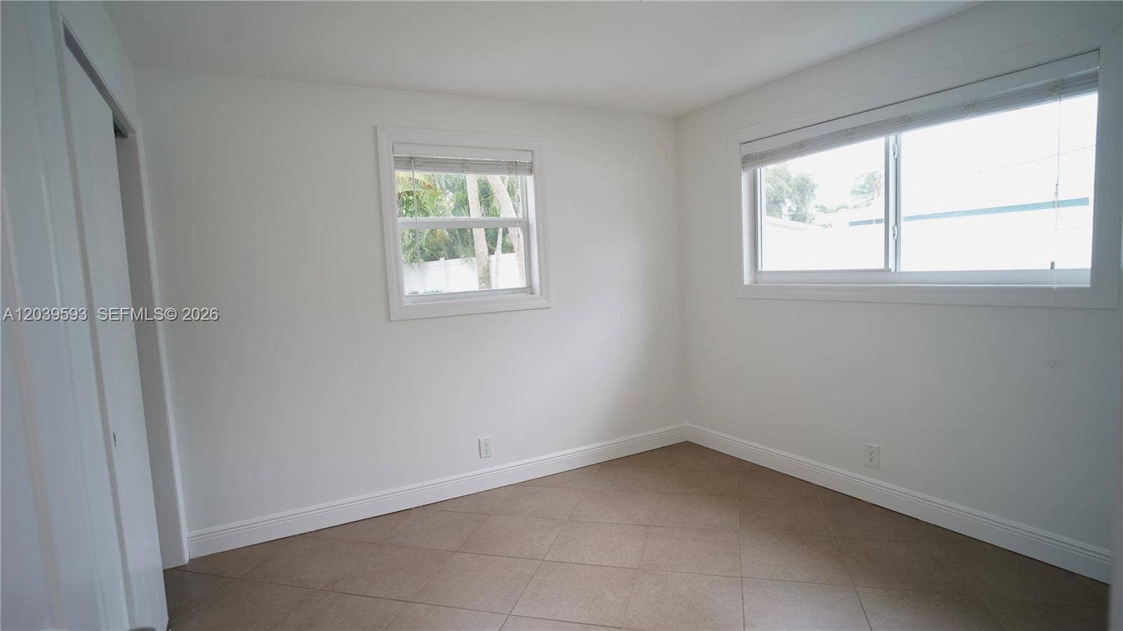Neutral-toned interior space featuring large-format tile flooring, dual windows with installed blinds, and a built-in closet with sliding doors