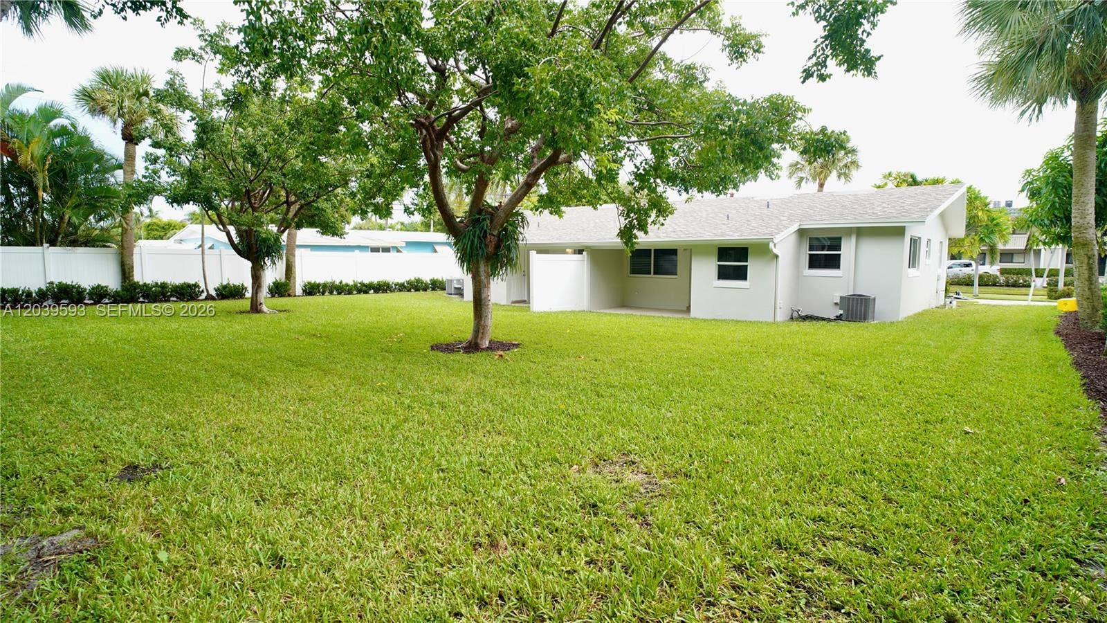 Expansive backyard featuring a sprawling lawn, mature shade trees, perimeter privacy fencing, and a covered concrete patio