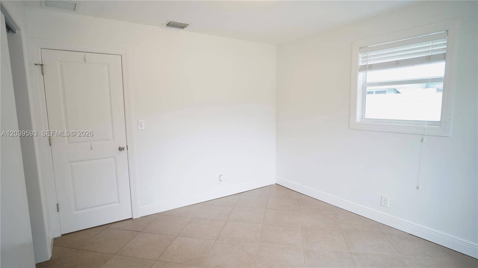 Interior room featuring neutral-toned tile flooring, white-painted walls, a single-panel interior door, and a horizontal window with white blinds