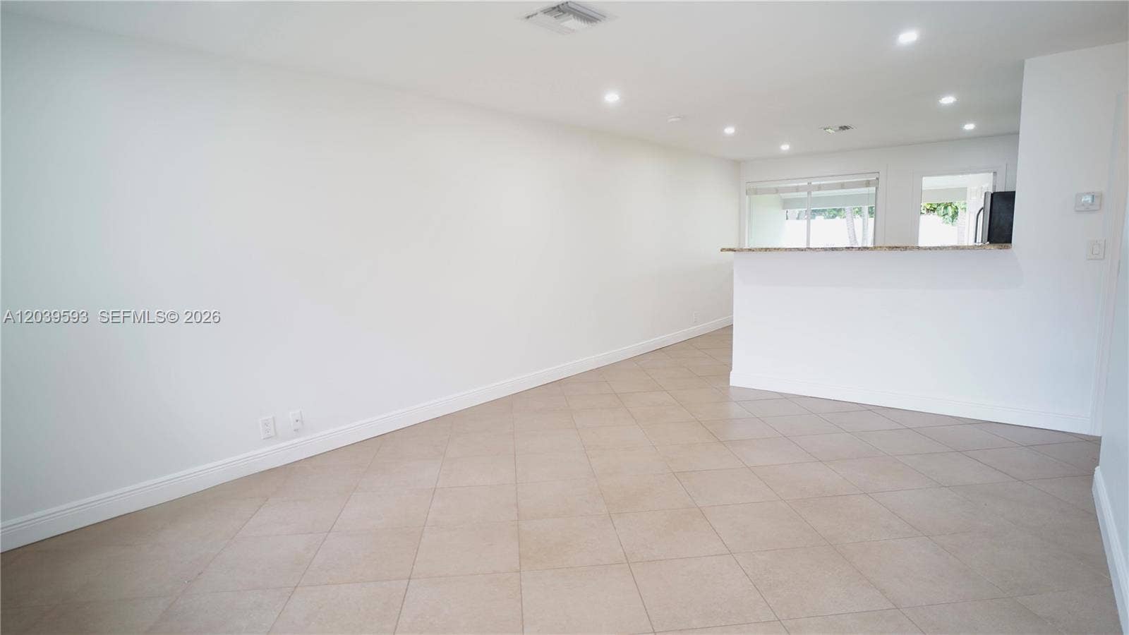 Open floor plan featuring neutral large-format tile flooring, recessed ceiling lighting, and a stone-topped breakfast bar