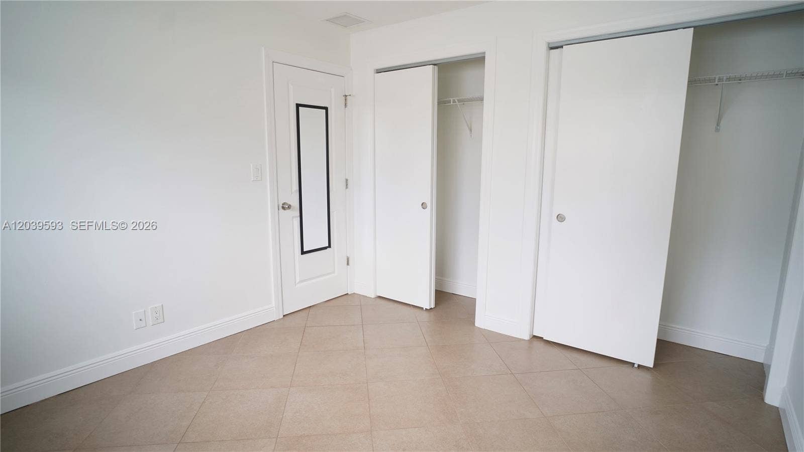 Neutral-toned tile flooring, two closets with white panel doors, and a single interior door featuring a built-in vertical mirror