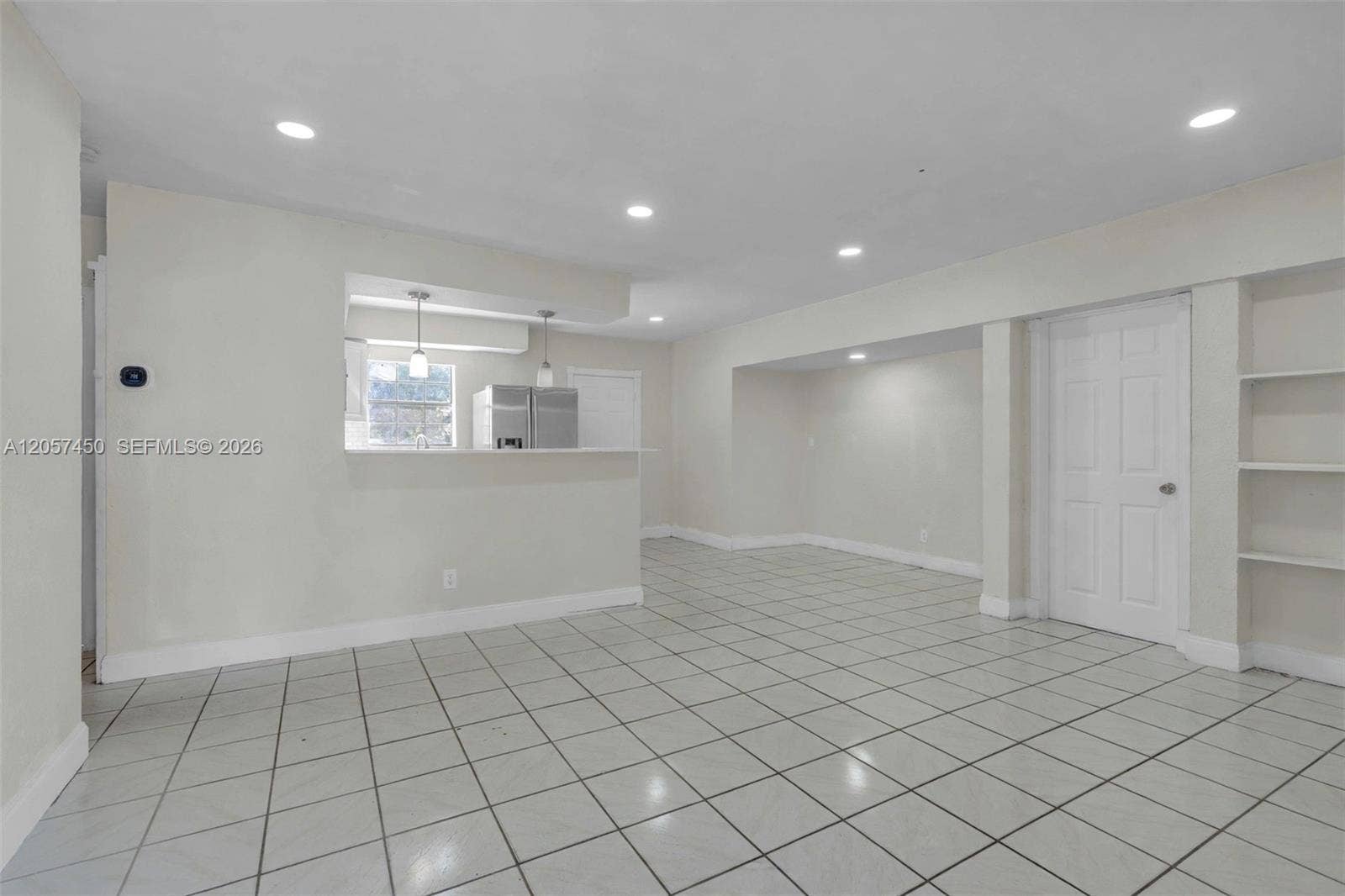 Open interior space featuring light-colored tile flooring, recessed lighting, a built-in shelving unit, and a pass-through opening