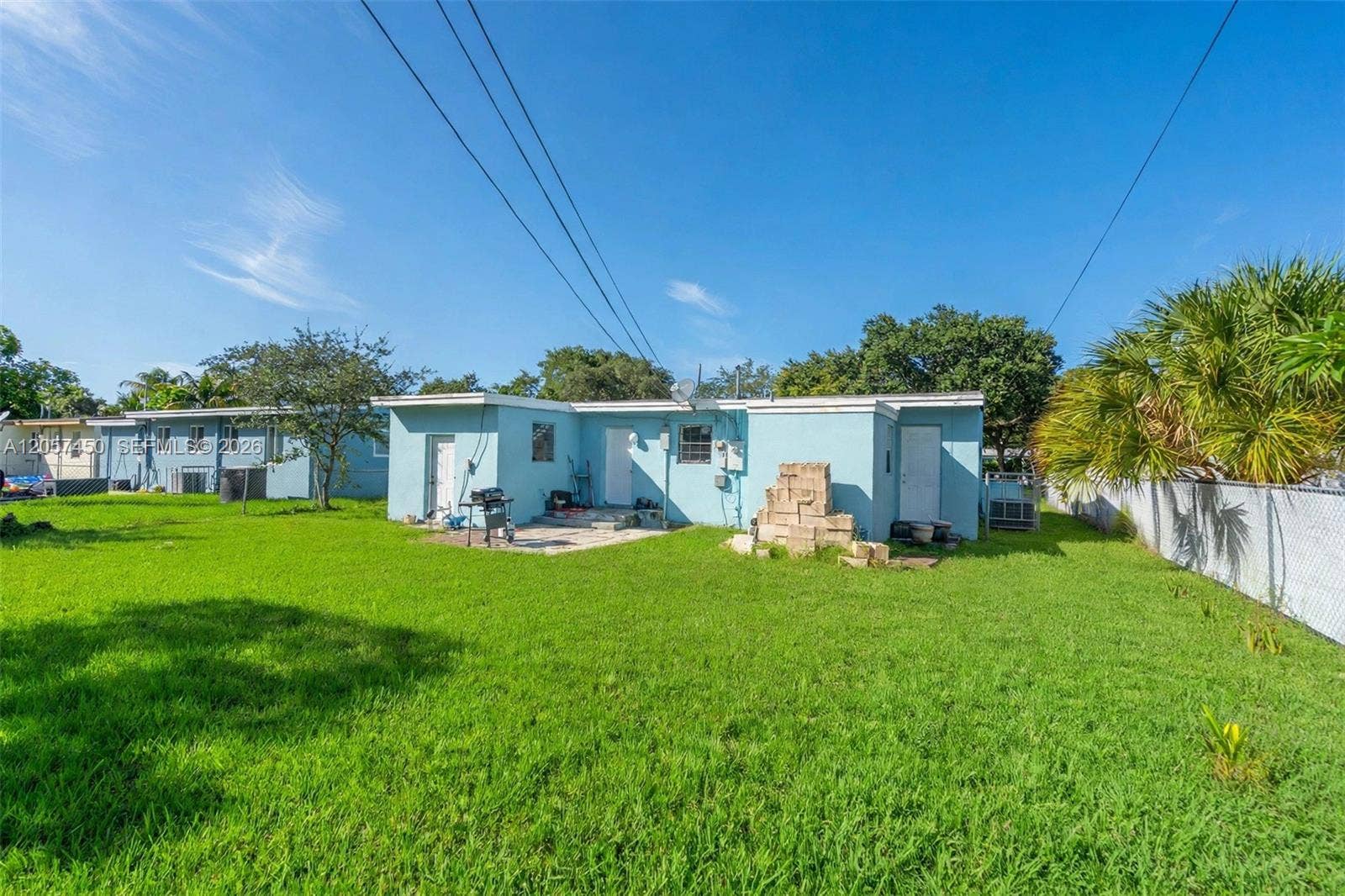 Spacious backyard featuring a grass lawn, paved patio area, chain-link fencing, and mature trees