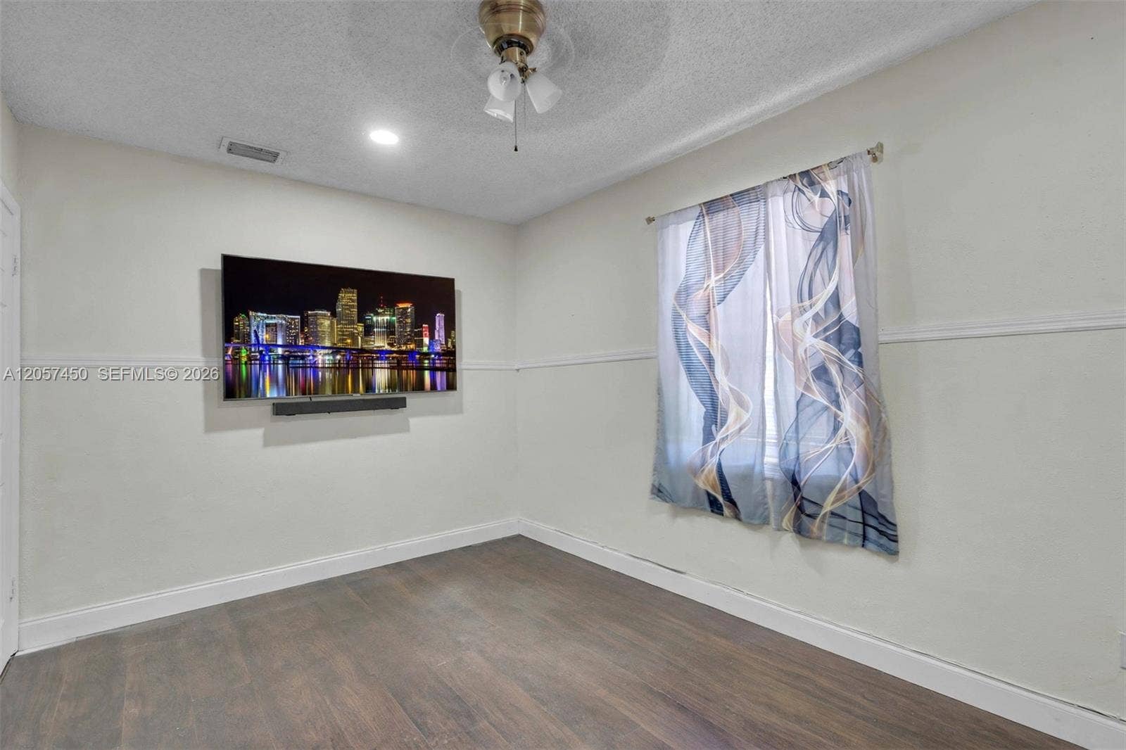 Room featuring wood-finish flooring, chair rail molding, a textured ceiling, and a central ceiling fan with integrated lighting