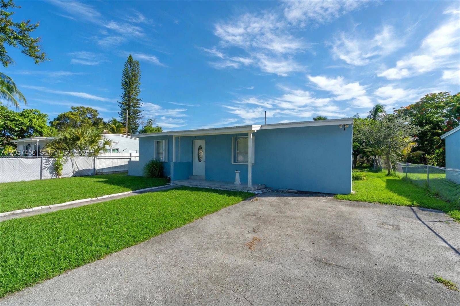 Single-story exterior featuring a painted stucco finish, covered entryway, paved driveway, and expansive lawn
