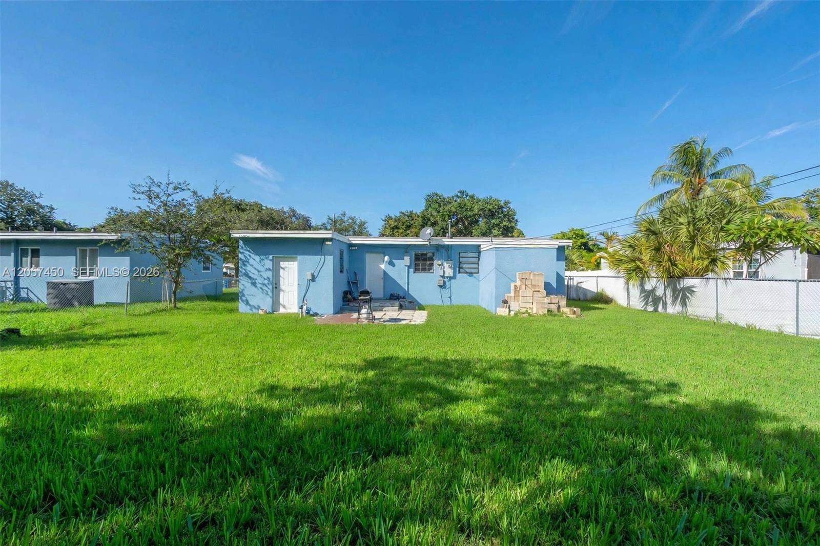 Expansive backyard featuring a large grass lawn, perimeter chain-link fencing, mature trees, and a blue exterior finish