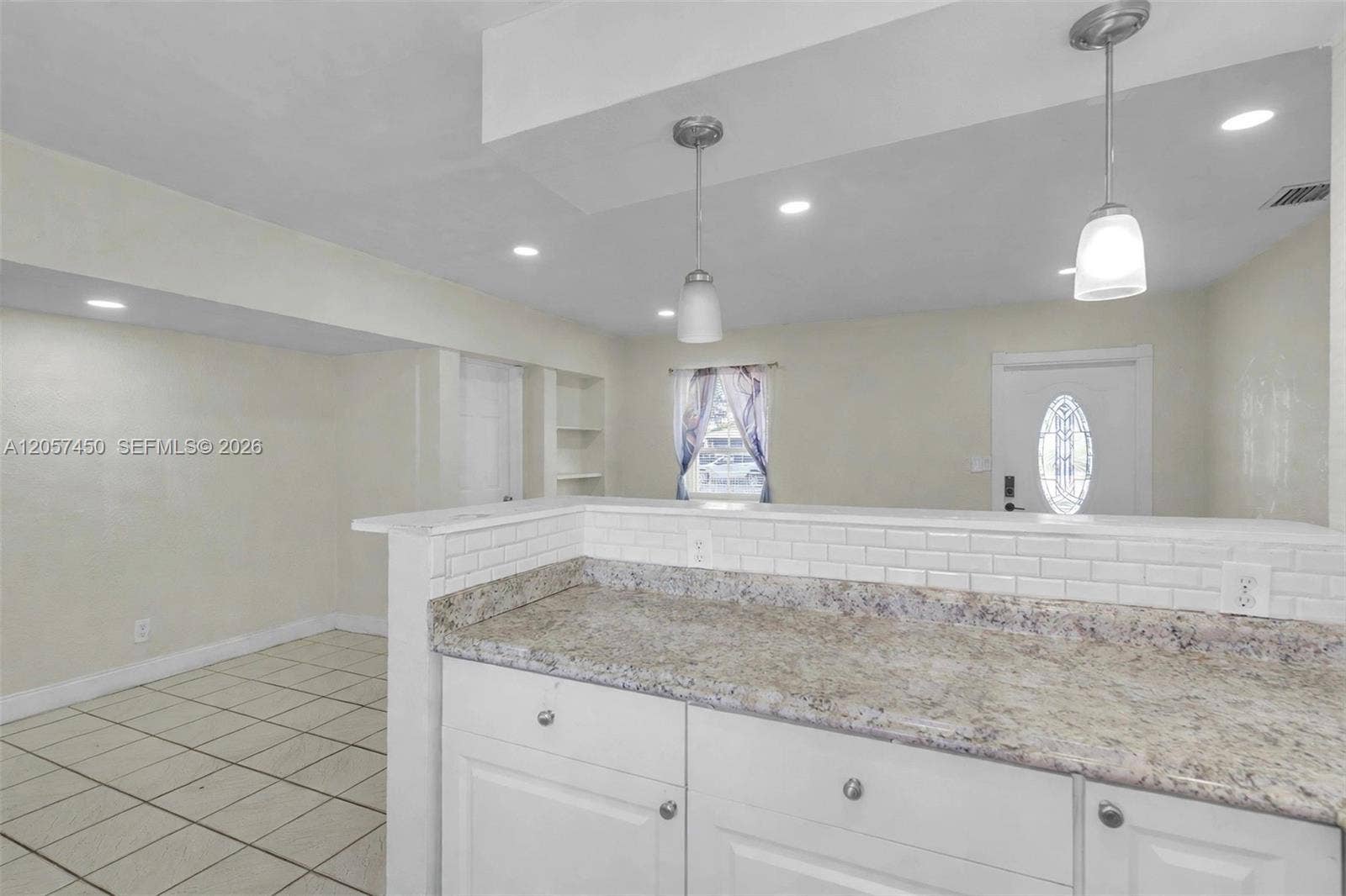 Kitchen featuring a stone-look countertop, white subway tile backsplash, white shaker-style cabinetry, two brushed-nickel pendant lights, and tile flooring