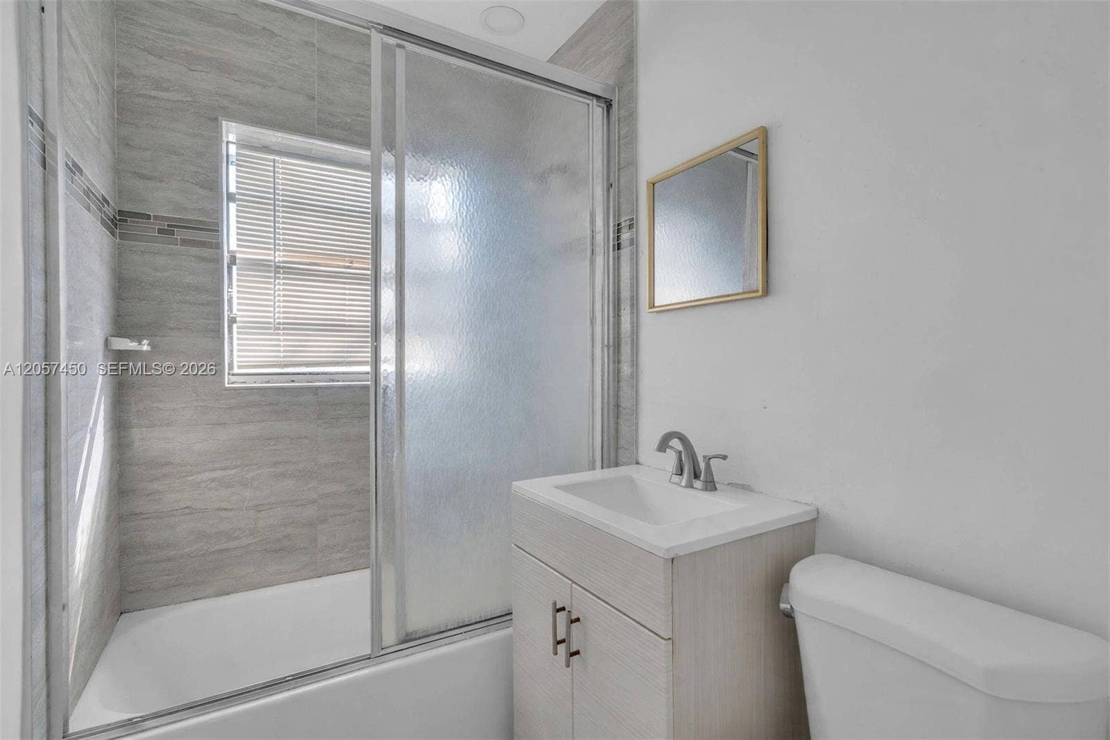 Bathroom featuring a shower-tub combination with sliding glass doors, horizontal tile wall surround, wood-finish vanity with a rectangular basin, and metal faucet hardware