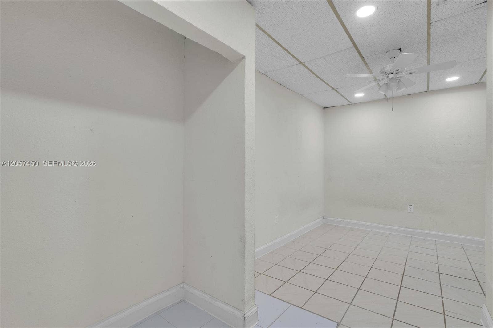 Interior space featuring neutral wall tones, white floor tiles, a drop ceiling with recessed lighting, and a white ceiling fan with integrated light fixtures