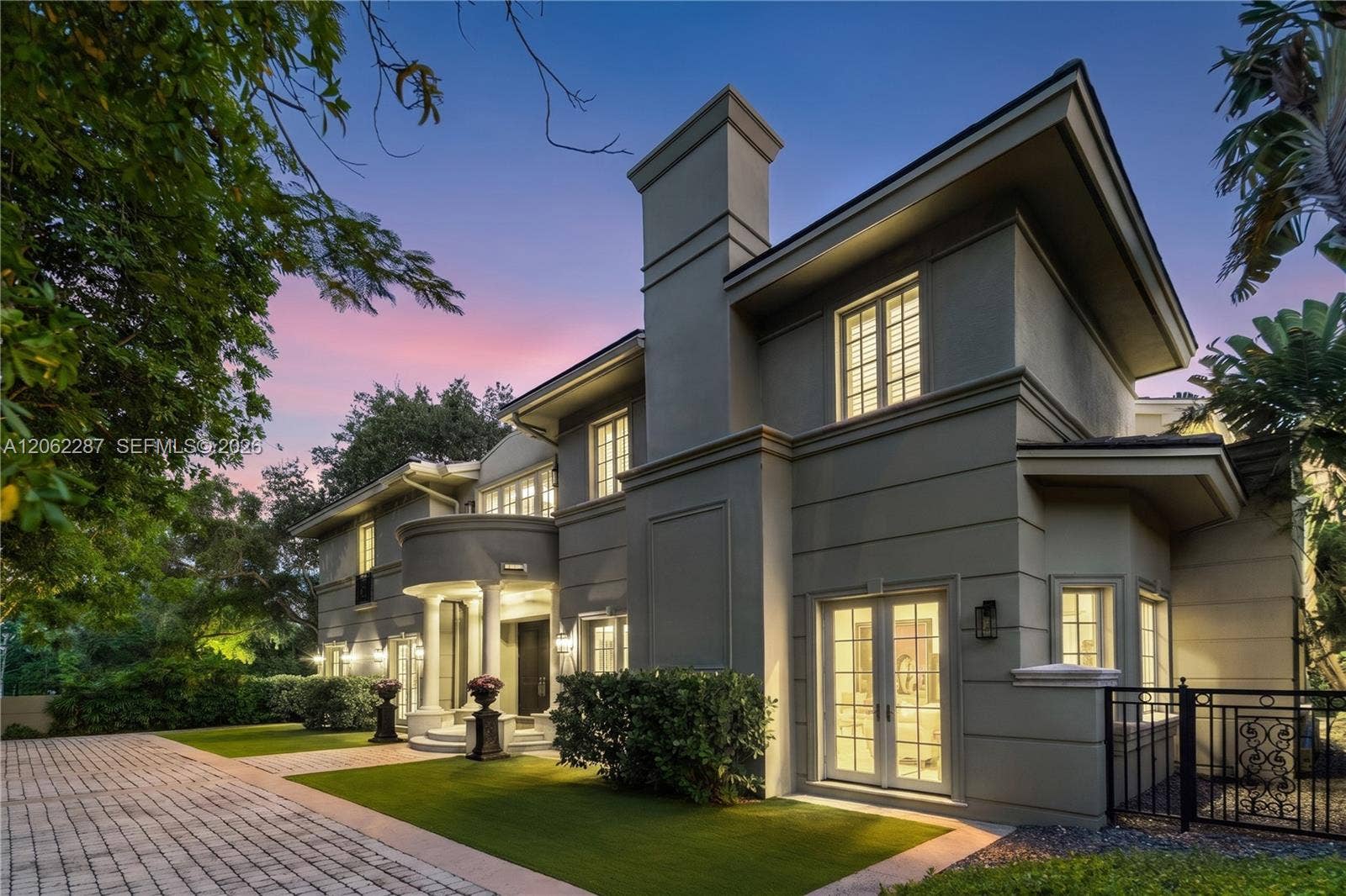 Two-story exterior featuring a stucco facade, a pillared entryway with a curved balcony, multi-pane windows, and a paved driveway