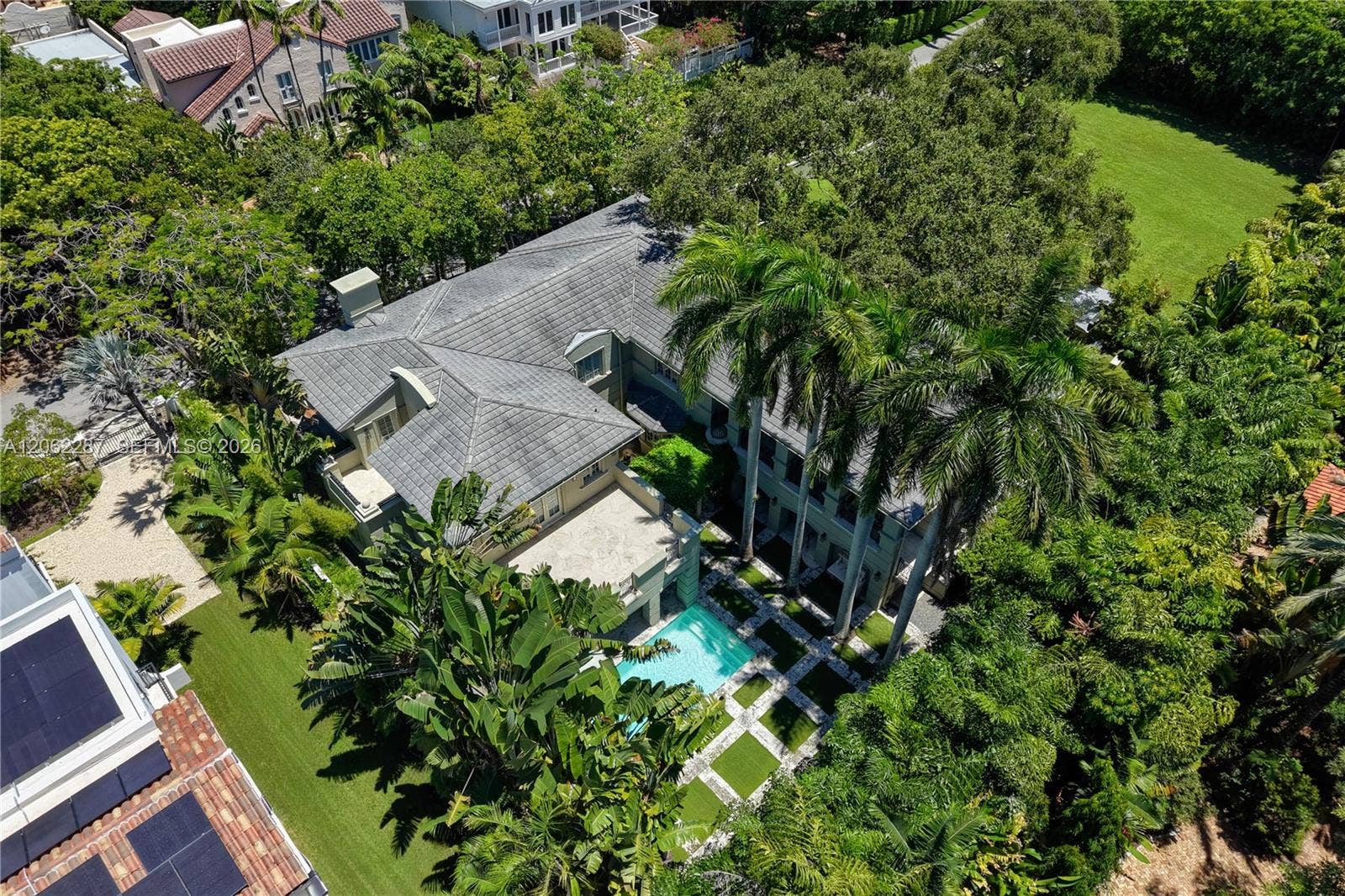 Aerial perspective of a multi-level estate featuring a tile roof, an in-ground swimming pool, stone-paver hardscaping, mature landscaping, and an expansive lawn